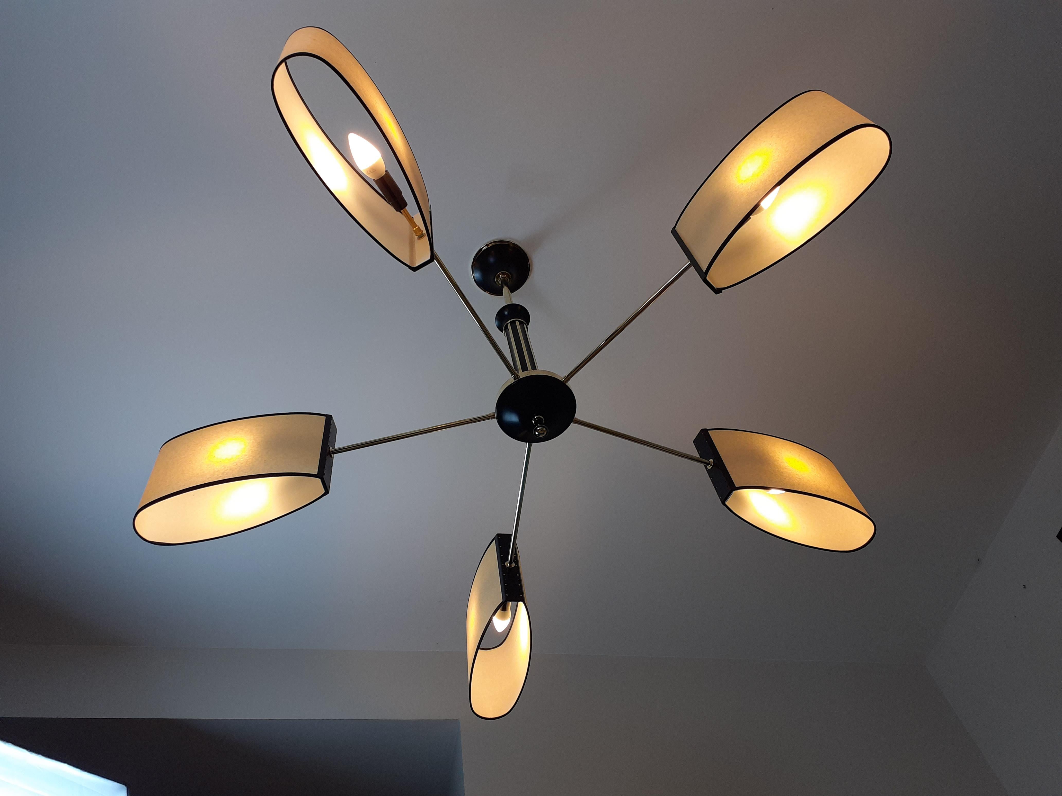 Circular chandelier in brass and lacquered metal, composed of a cylindrical chest in black lacquered metal with brass net holding a base on which are fixed five brass light arms terminated by black lacquered perforated metal plates supporting oval