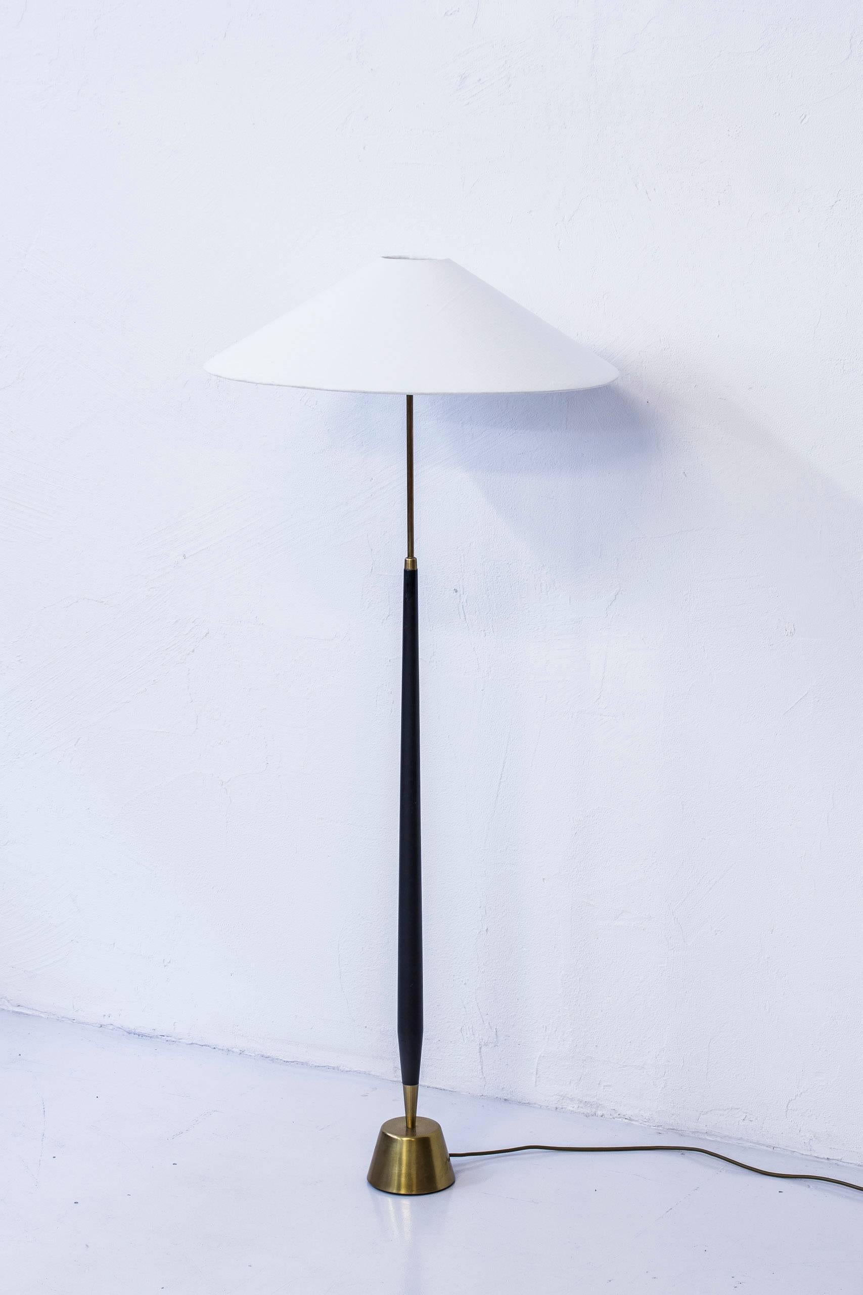 Floor lamp produced in Sweden during the 1950s by ASEA Belysning. Made from black lacquered wood and polished brass. With a heavy cast iron weight in the base. Lampshade in off-white, textured linnen fabric. Original light switch on the lamp fixture