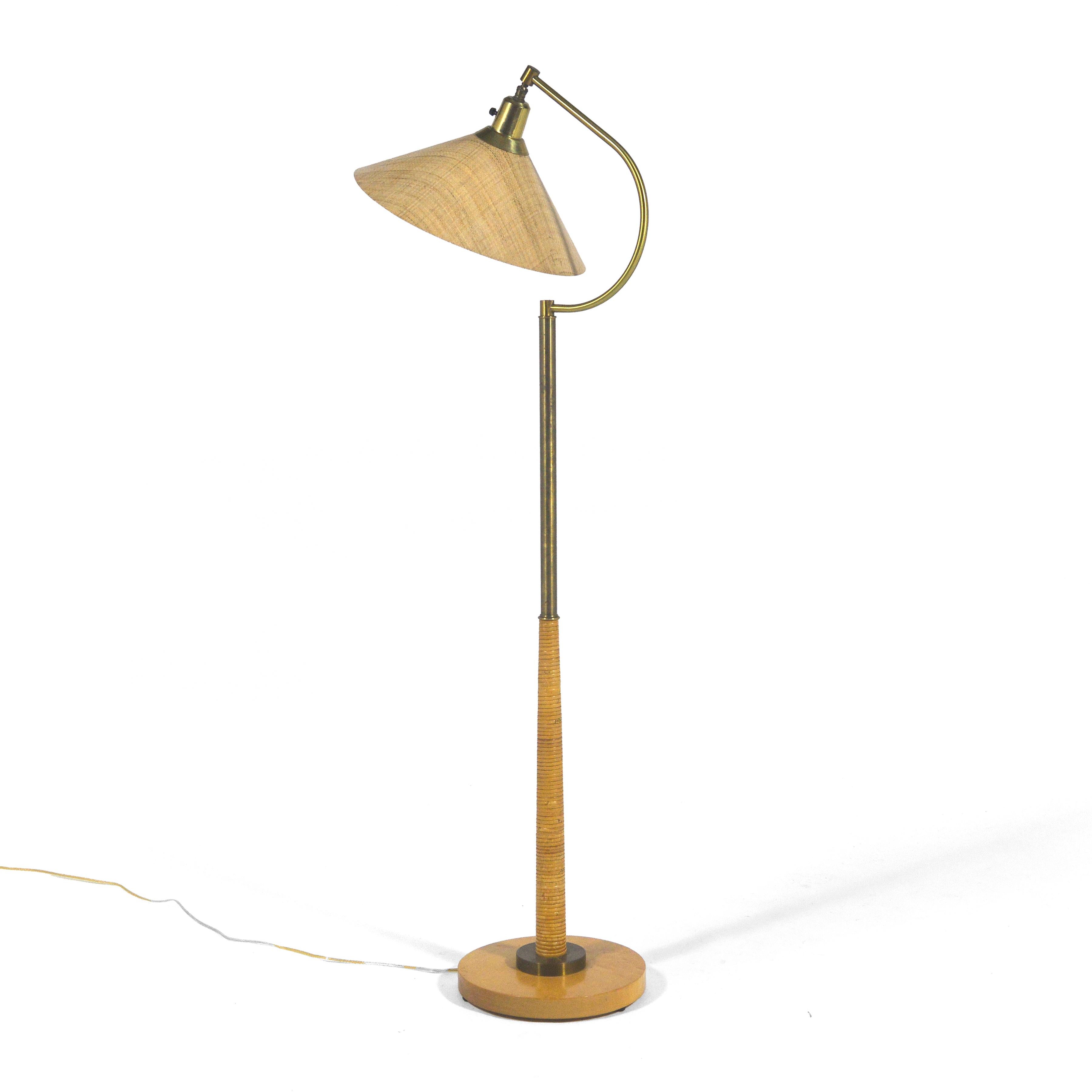 This lovely lamp executed in brass with several delightful design details including the wood base, the cane wrapped column, and the rafia-ware style shade.

Offering both directional and ambient lighting, the lamp has a sculptural presence while