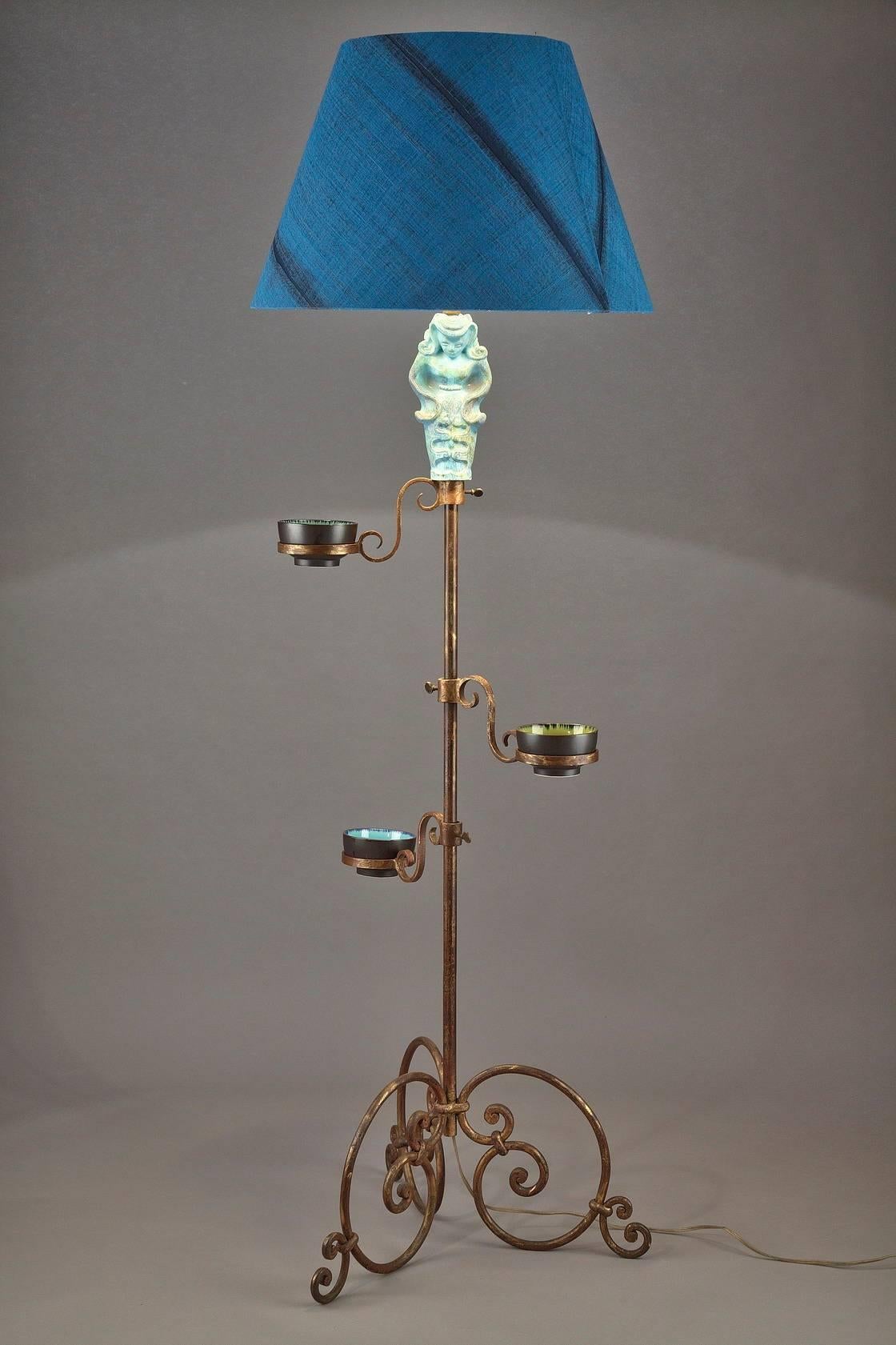 Wrought and gilded iron floor lamp, the stem decorated with a blue ceramic figure and three blue and green small bowls. It is resting on three scrolled feet. 

circa 1950.
Dimension: L 60cm, P 60cm, H 180cm.

  