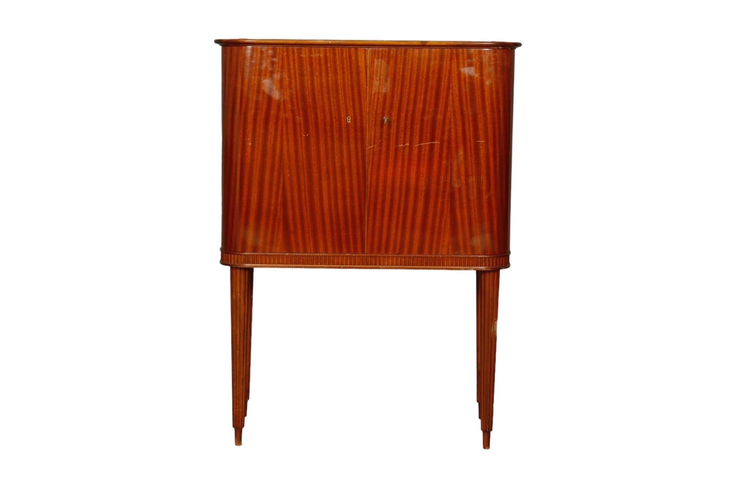 1950’s Bar cabinet by Förenades Möbler of Linköping, Sweden. An inset demilune clouded glass panel sits on top of the lighted bar. Locking bentwood cabinet doors, decorated in flame mahogany veneers, have two and three shelves for glassware. Inside