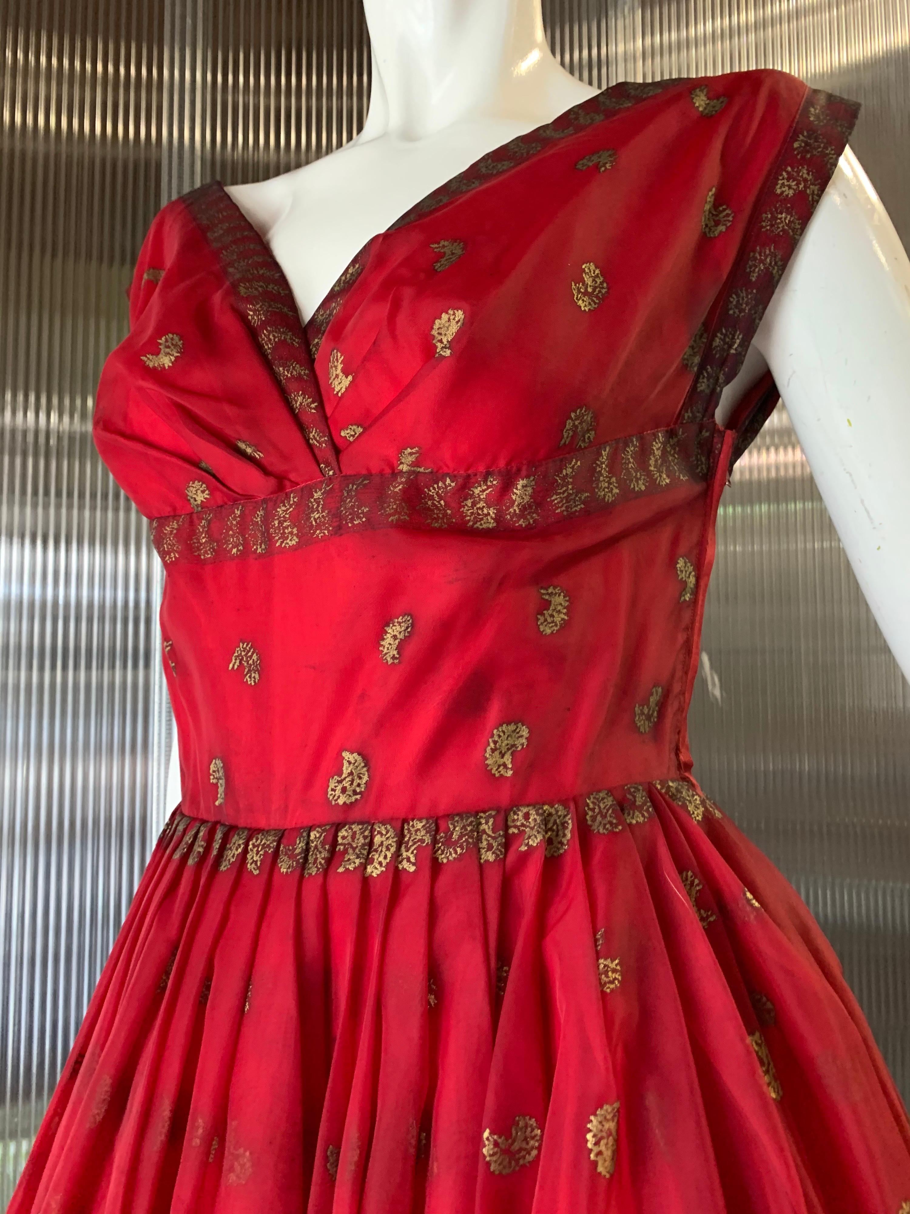 1950s Fred Perlberg Indian-Inspired dancing dress in crimson nylon organza and gold metallic paisley stamped pattern with 2 layers of lining. Fitted bodice and full pleated skirt. Side zipper. Fits a modern size 6.