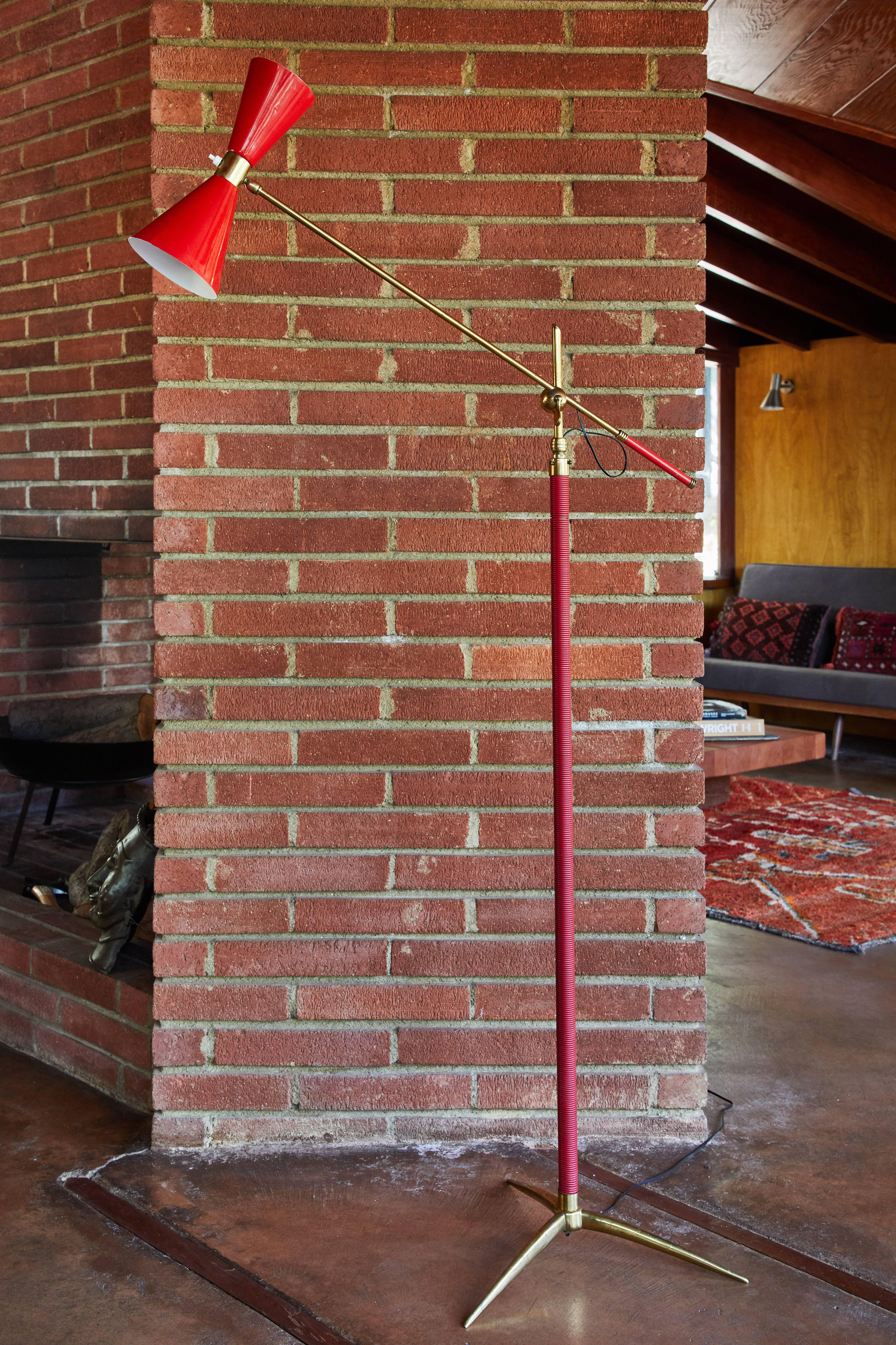 1950s French articulating floor lamp. Executed in red painted metal, red vinyl and brass. An interesting amalgam of the styles of Arteluce, Kalmar and Lunel, this floor lamp is highly sculptural with its brass tripod base and elegant articulating