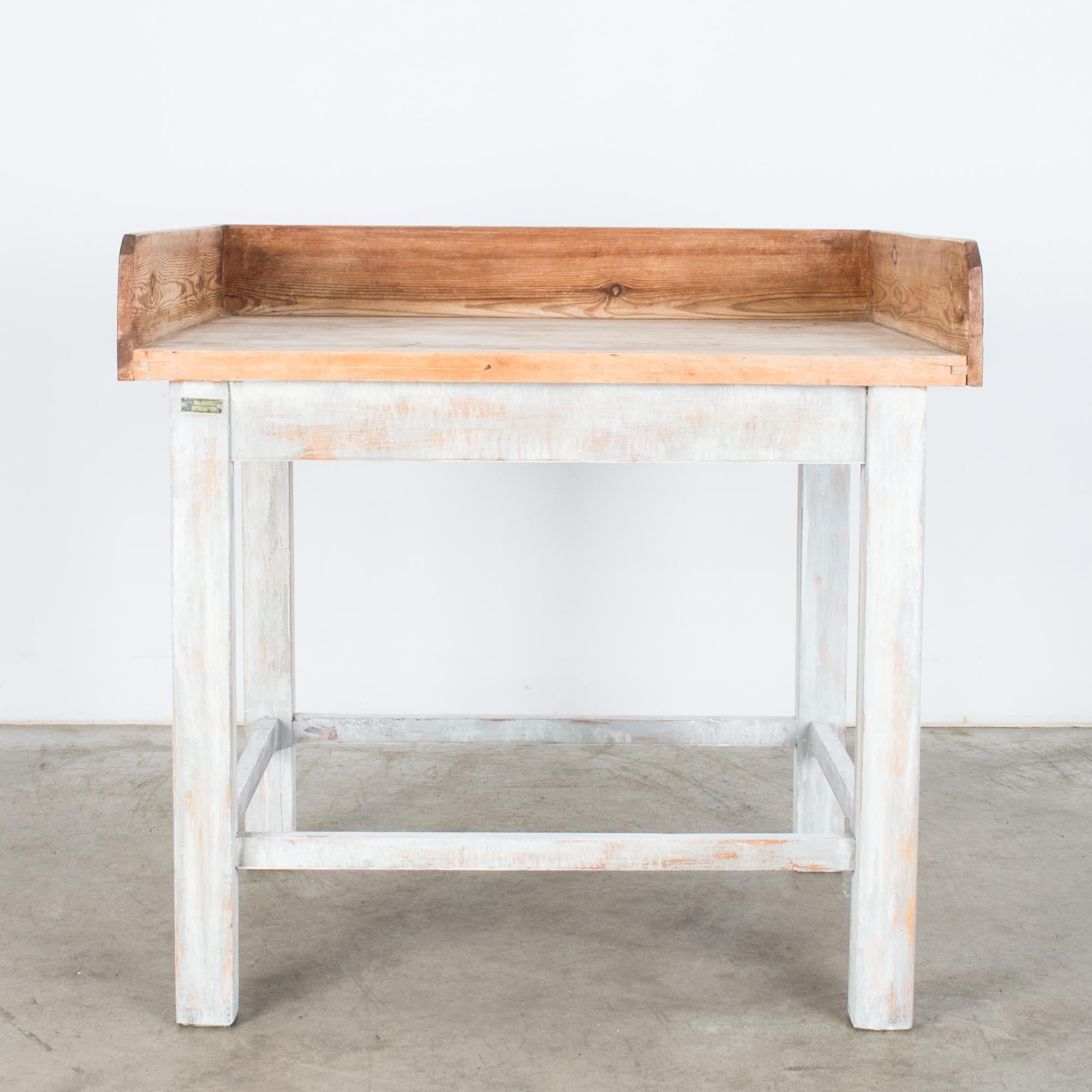 A rustic bakery table from 1950s France. A natural wooden benchtop creates an ideal workspace, with raised sides to prevent scattering and spills. The wood has a rich auburn hue, worn cloudy on the surface of the worktop, while a wash of white paint