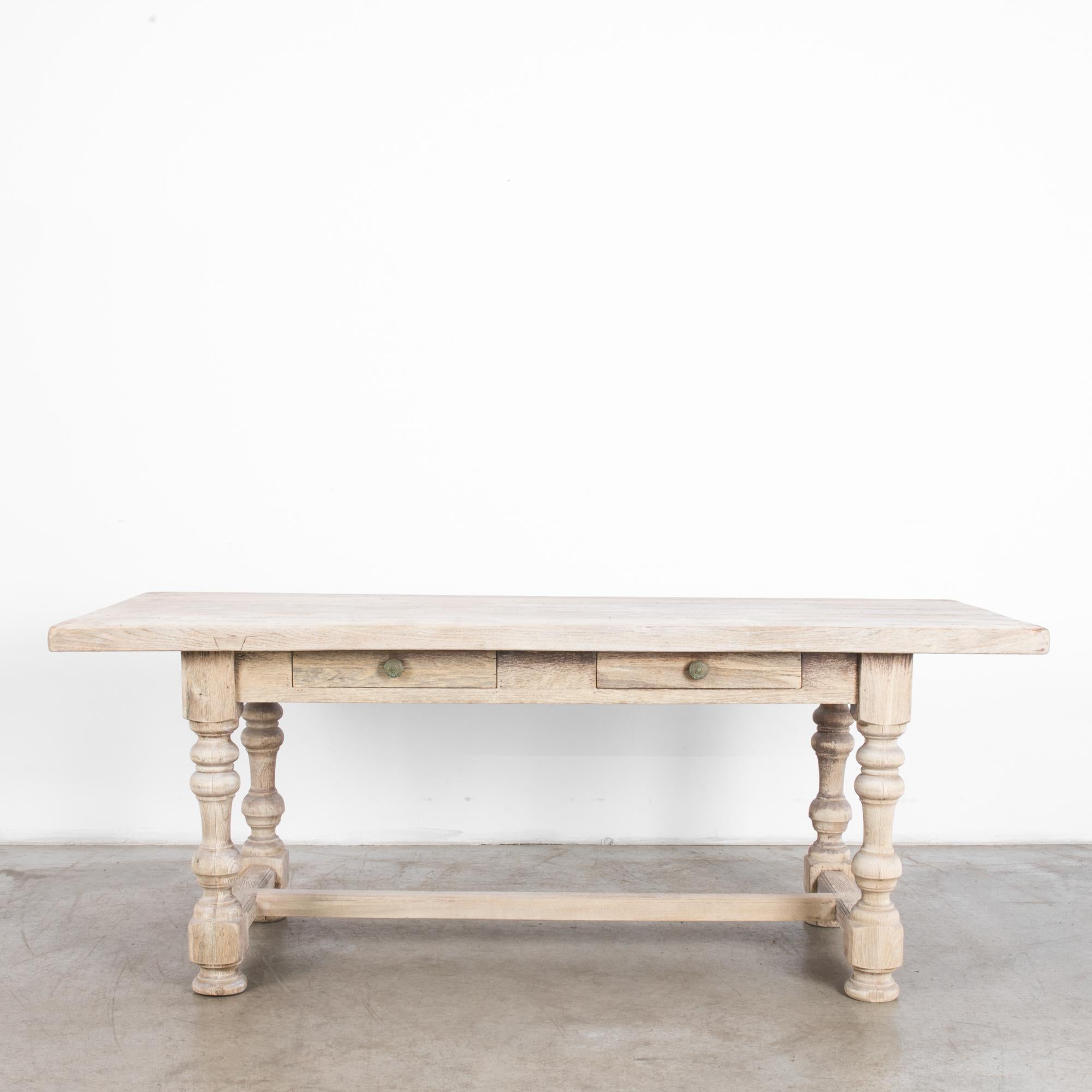 A wooden dining table from 1950s France, made of bleached oak. Sturdy turned table legs support a broad tabletop. A square apron hosts two small drawers. With the robust proportions of countryside practicality, a bright bleached oak finish gives