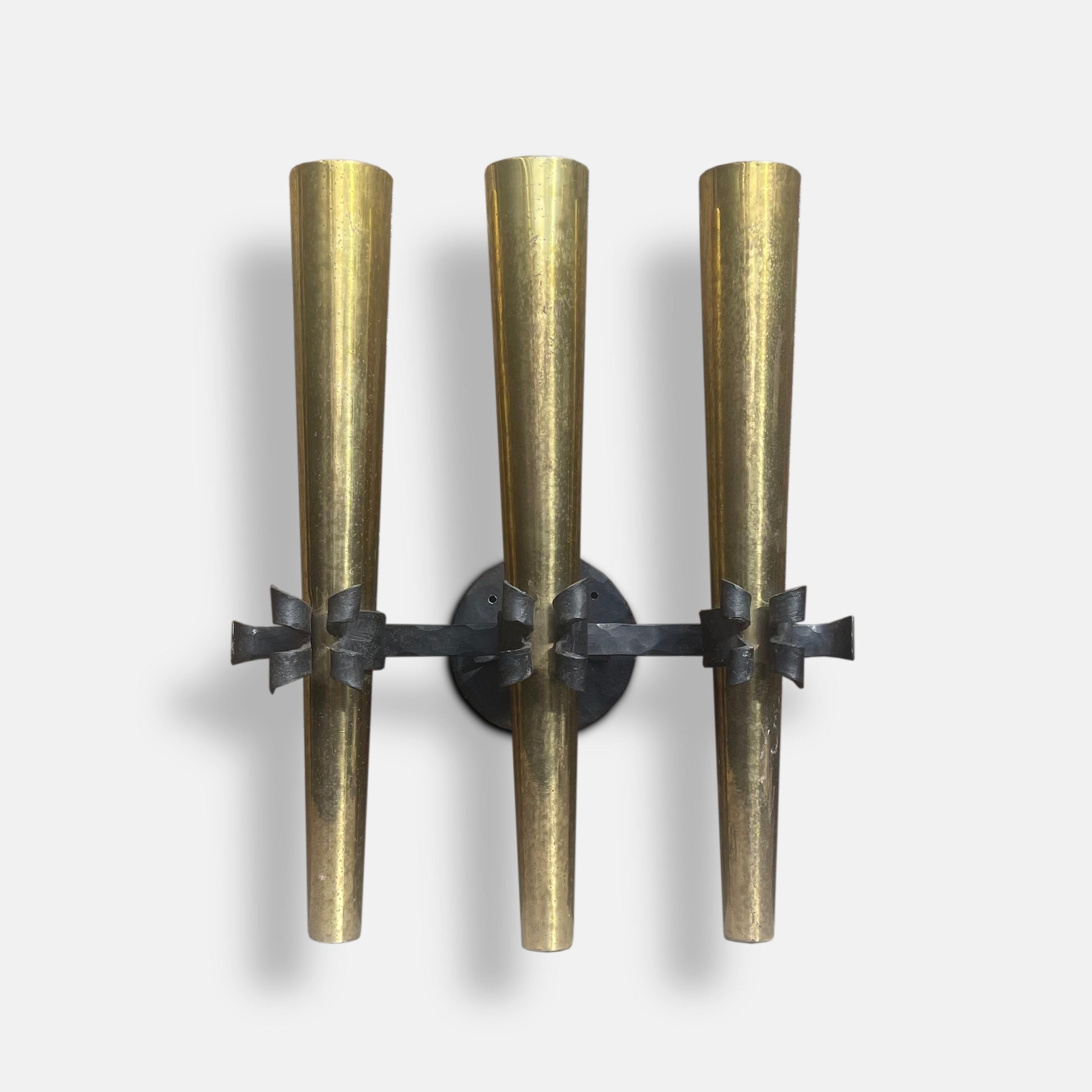 With three tubed brass torches, held in place by the decoratively ribboned arms of its hand-forged wrought iron fixture, this torchière wall sconce is a dramatic piece of French 1950s design.

Dimensions: D 17.6cm W39.2cm x H 45.5cm.