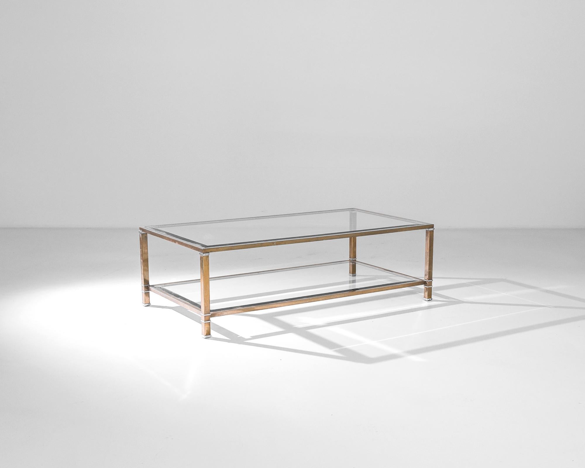 Made in France circa 1950, this coffee table displays an elegant silhouette. Sleek materials and details– plated brass and bevel cut glass– emphasize the Midcentury chic. A metallic structure, supporting two glass shelves, provides an industrial