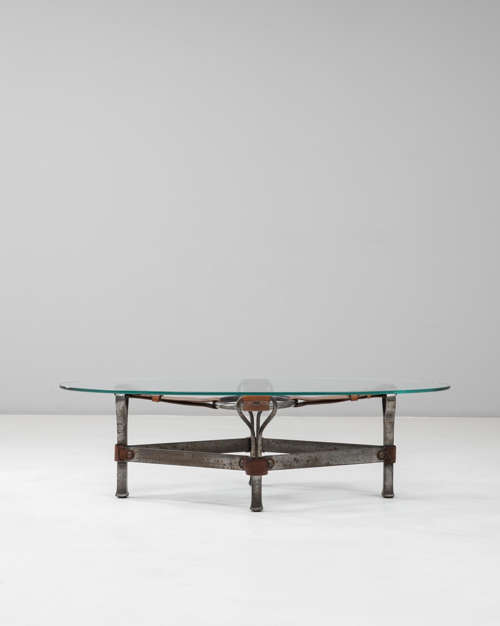 Cette table basse en verre de Jacques Adnet, datant des années 1950, incarne l'équilibre entre la rigueur, l'honnêteté des matériaux et la retenue sculpturale qui caractérisent le designer. La base en métal forgé présente des lignes fortes et