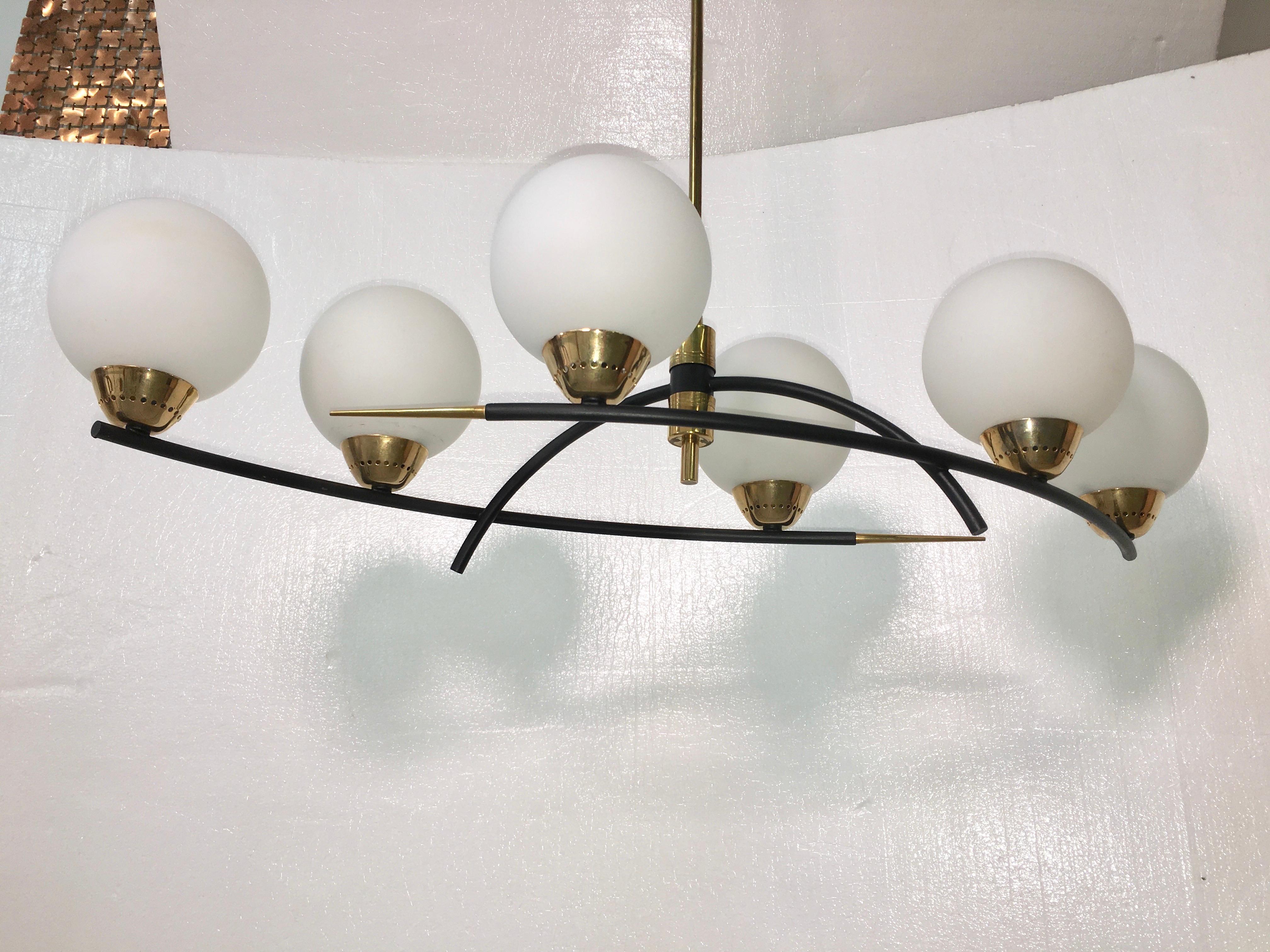 High quality and sculpturally Minimalist chandelier made of curved black enameled tubular brass embellished with solid brass finial spikes and having six brass bobeches holding six round satin opaline globes with candelabra bulbs inside. Rewired for