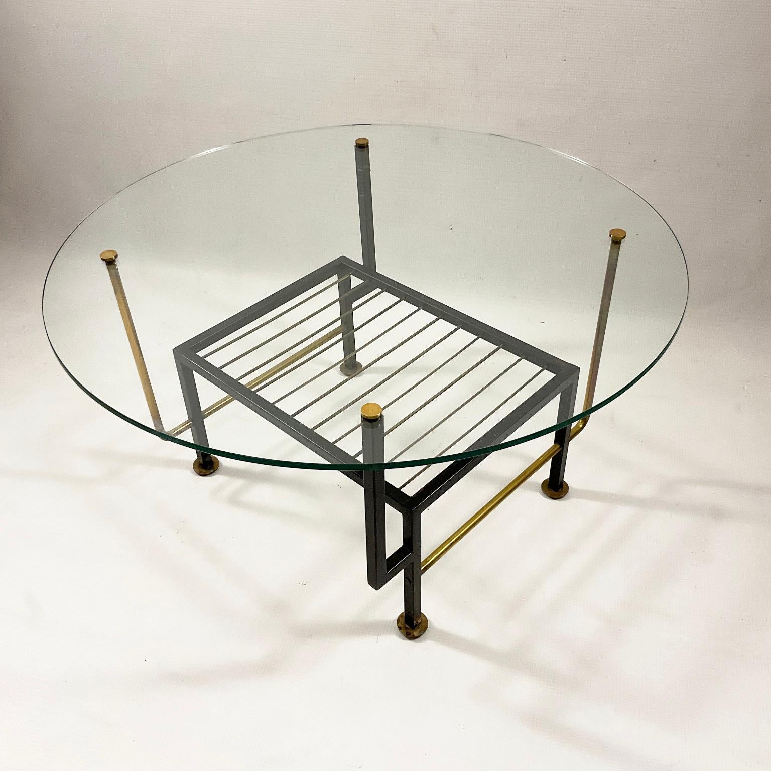 French coffee table from the 1950s with a magazine rack. 
Structure in brass and black enameled metal with its original round glass top. 
The shapes of this coffee table are reminiscent of certain creations by the famous French designer Mathieu