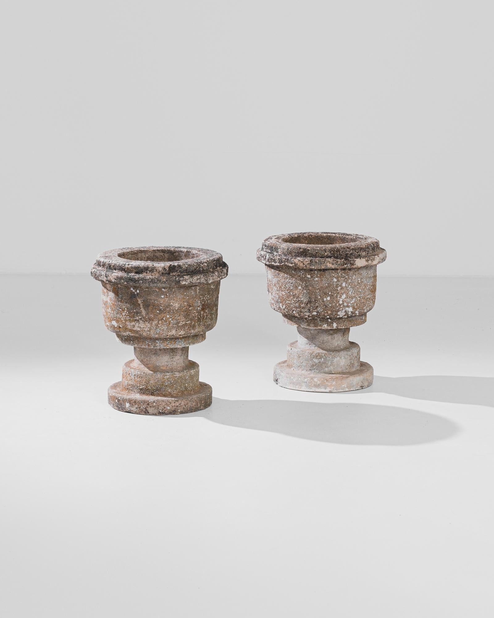 A pair of concrete planters from 1950s France. The symmetry of the rounded urn shape is doubled in the mirror-image of the twin forms. Minor variations in the finish of the natural concrete, weathered to a dappled color palette of lichen, peach and