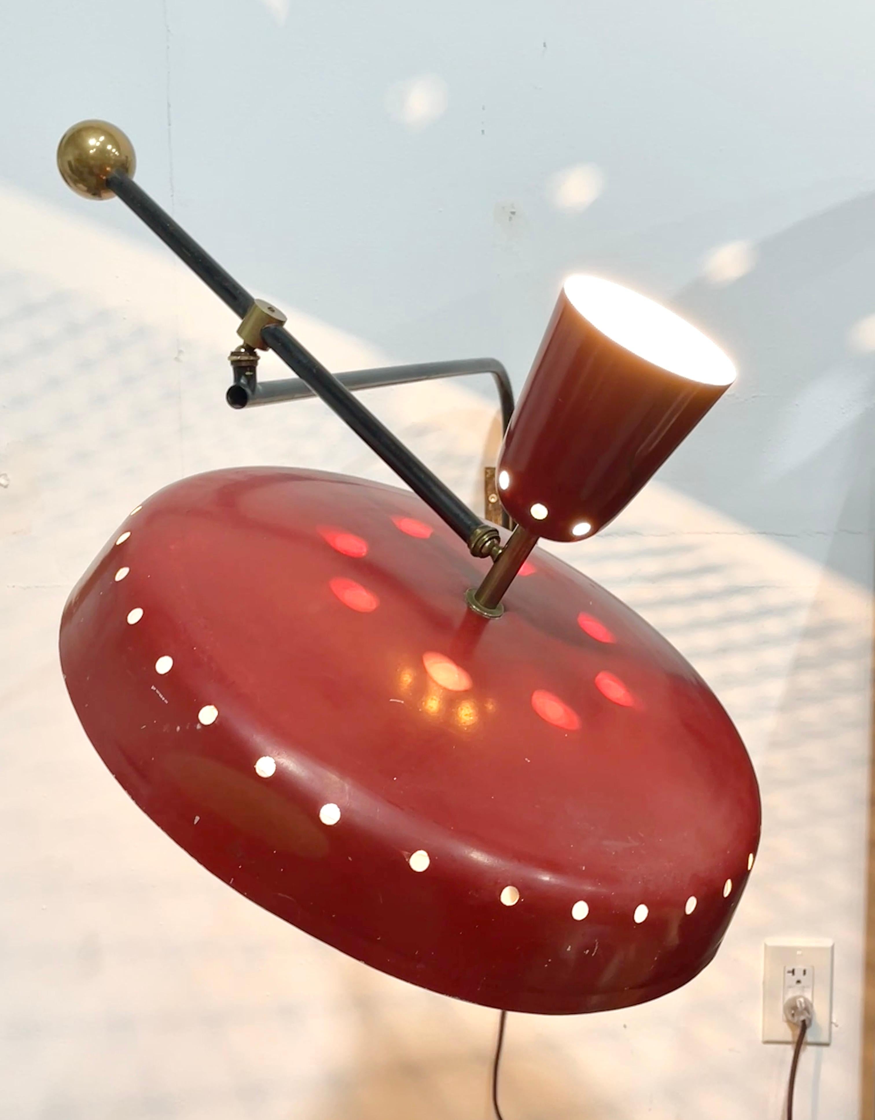Large scale French 1950's wall mounted swing arm lamp with a black enameled metal counterbalancing arm, large red shade made of red enameled aluminum dotted with round perforations, white enamel inside and a dome form metal mesh reflector screen