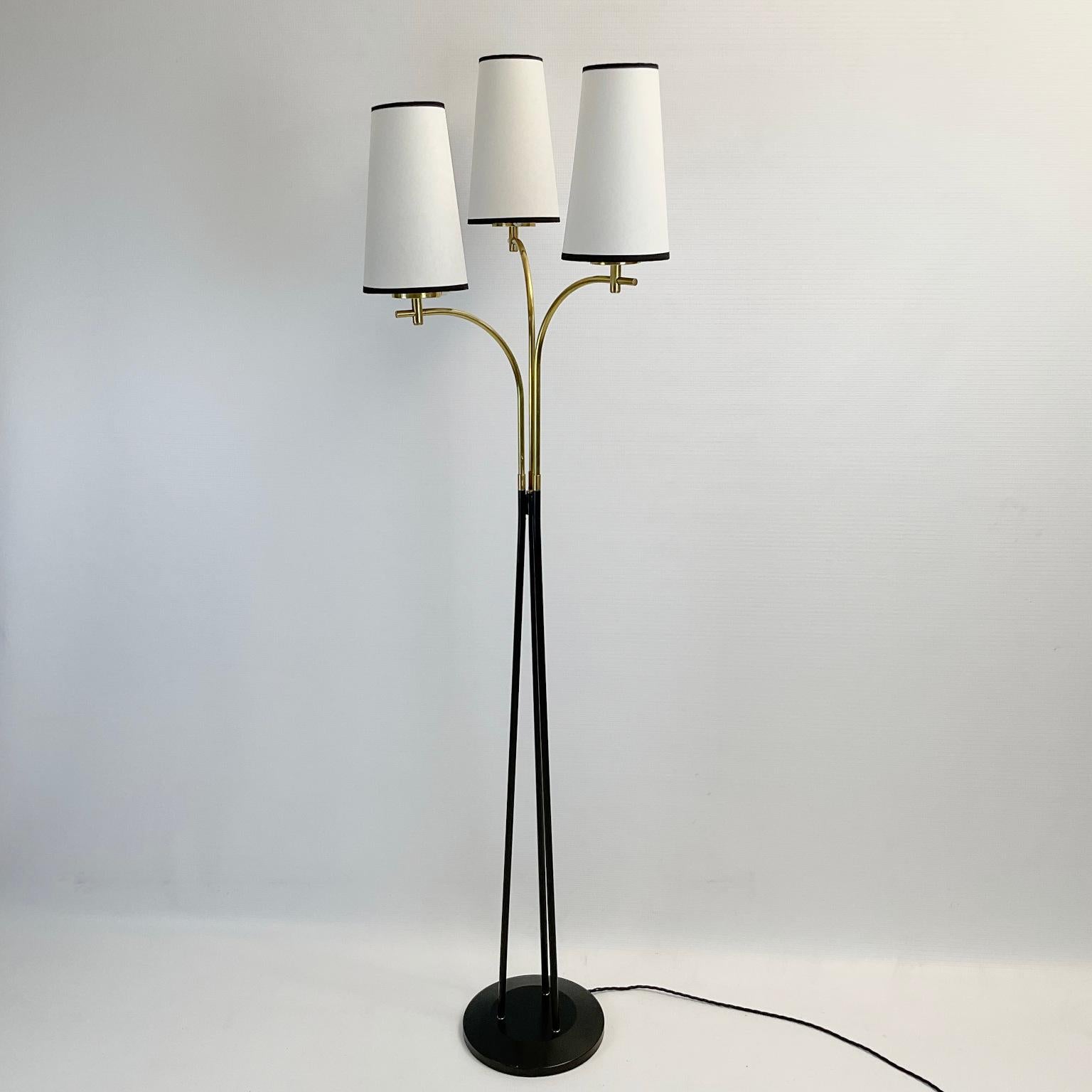 1950s floor lamp attributed to Maison Lunel France.
The circular base is painted black with a polished brass arm finish.
Each of the arms is topped with a parchment shade with a black trim ribbon.
At the base of each lampshade holder, there is a