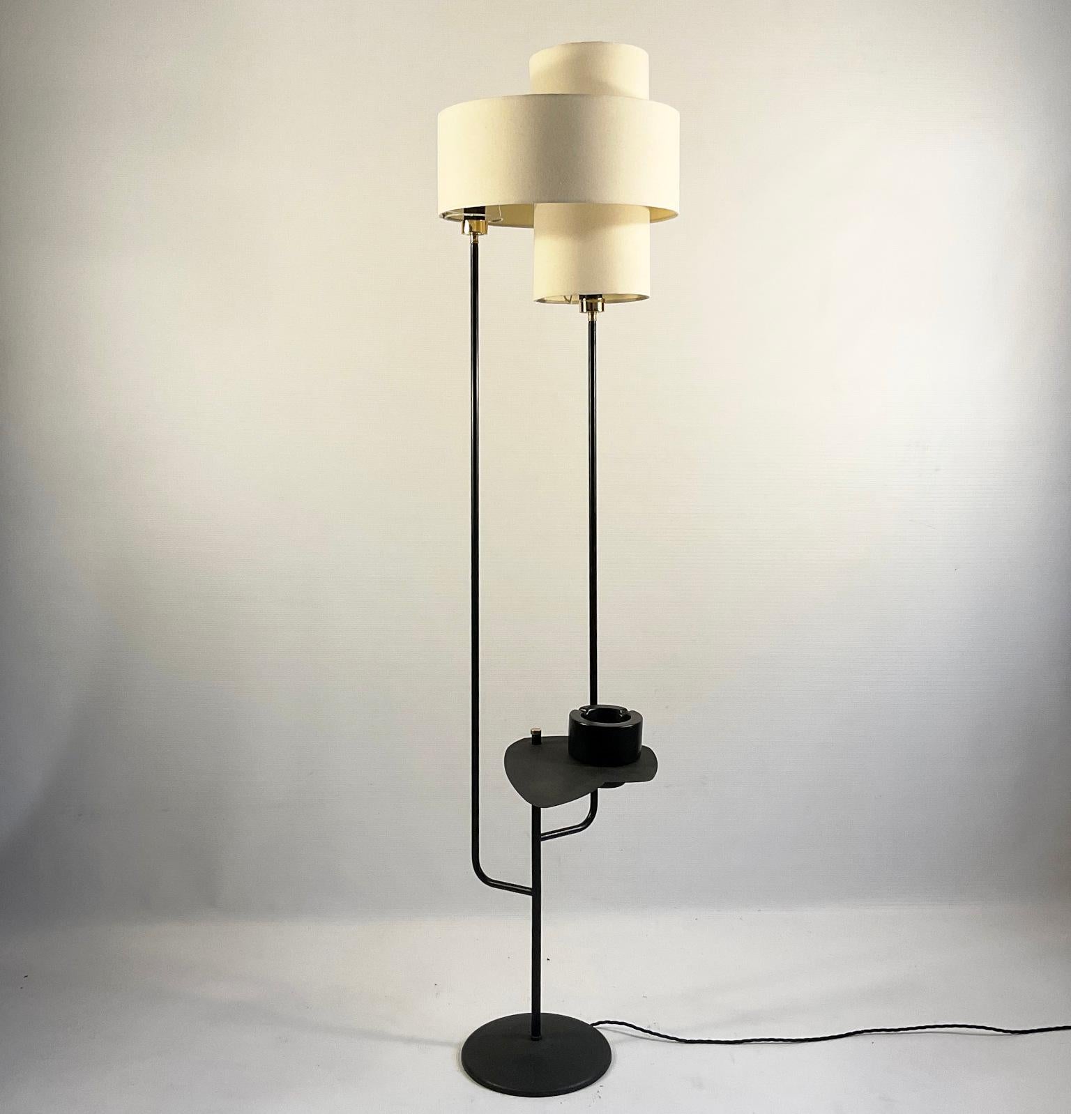 Französische Stehlampe aus den 1950er Jahren mit zwei Schirmen, die jeweils mit einem eigenen Schalter eingeschaltet werden können. Zur Stehleuchte gehört ein Beistelltisch, der nach Belieben verstellt oder entfernt werden kann.
Eine schwarz