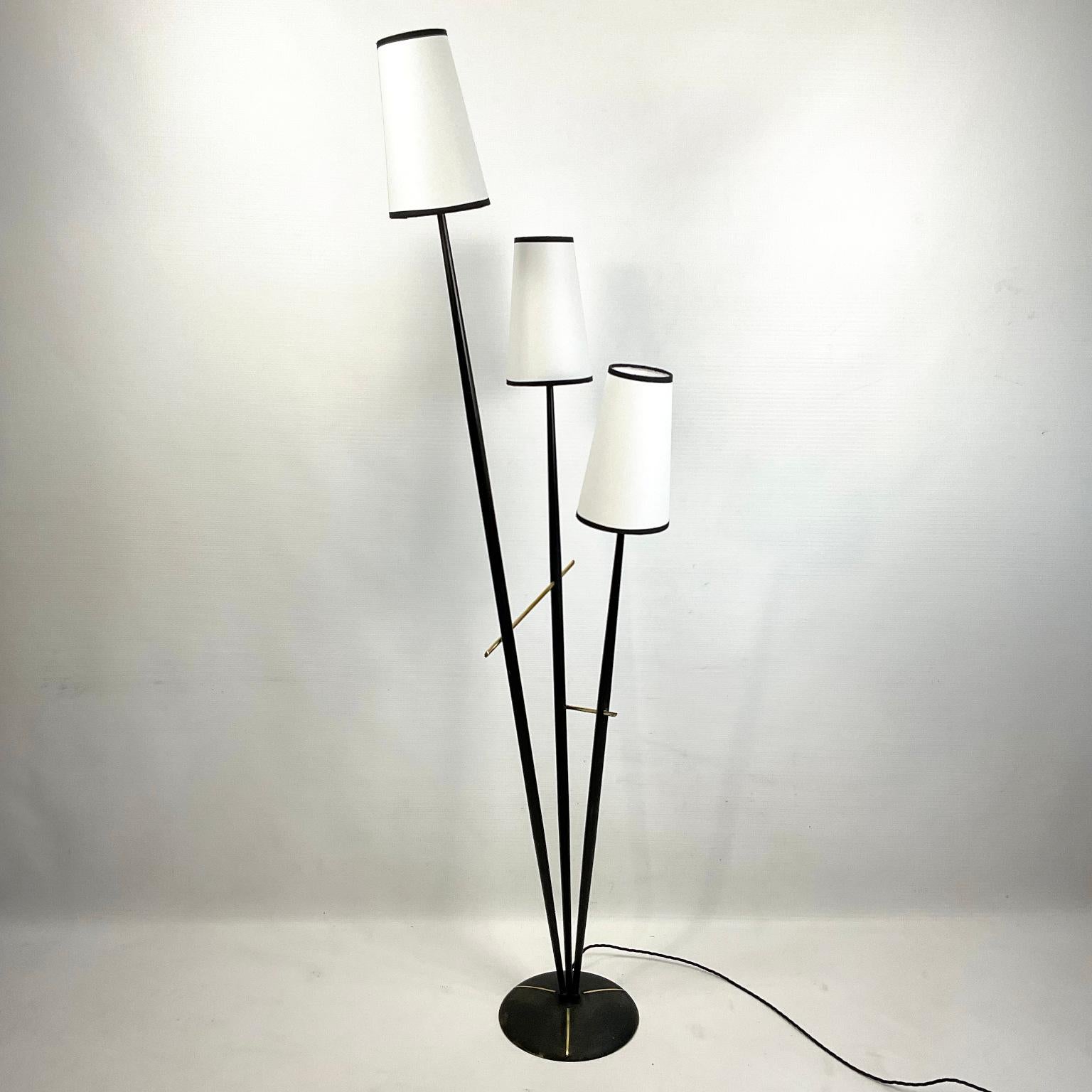 French Floor Lamp from the 1950s.
The circular base and the three branches are painted black with two polished brass crosspieces.
Each of the arms is topped with a parchment shade with a black trim ribbon.
At the base of each lampshade, there is a