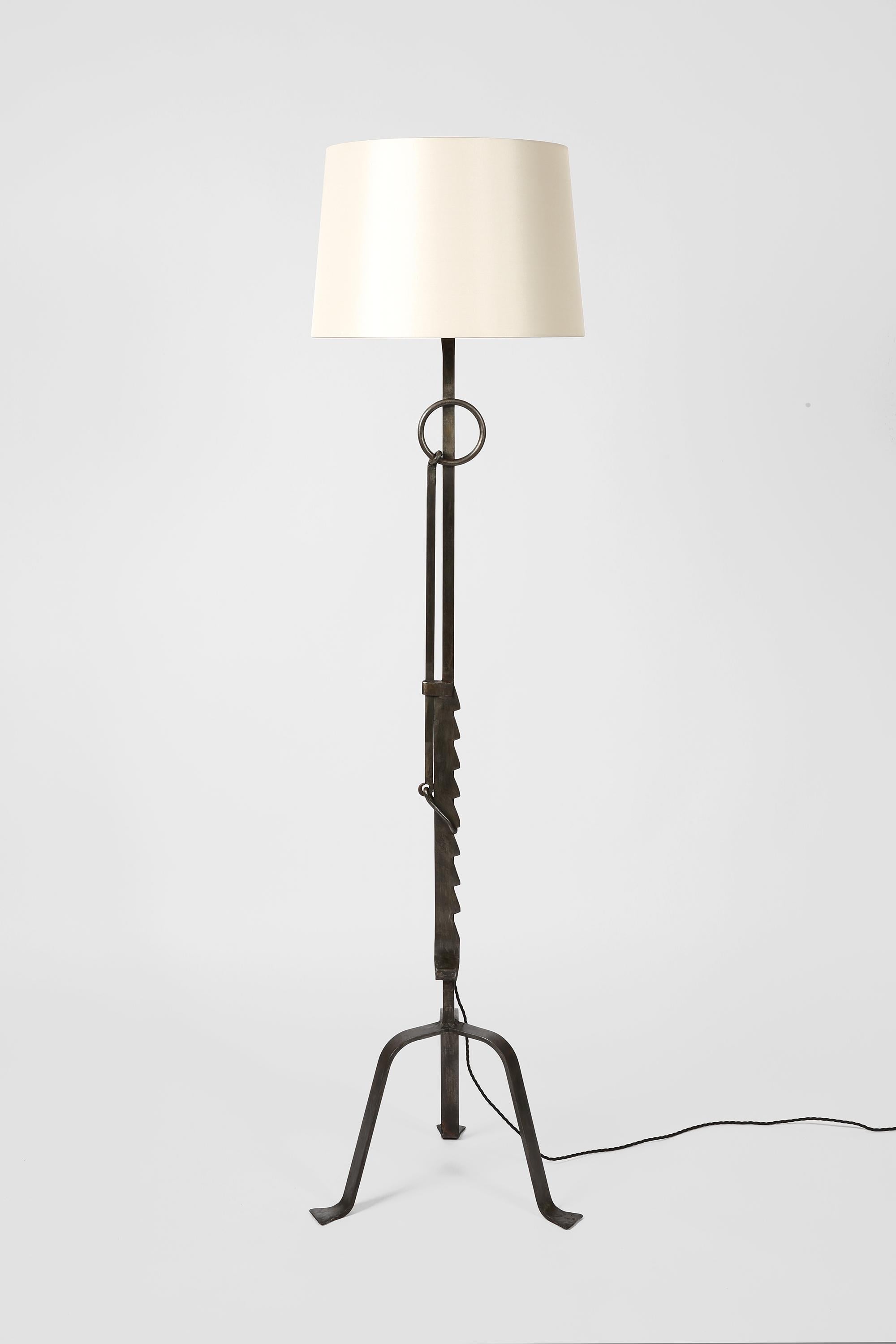 Una lampada da terra in ferro forgiato e saldato, in stile brutalista, formata in parte da antichi utensili domestici/agricoli - in questo caso una crémaillère. Opera d'arte popolare tipica della regione della Provenza. 

Fornito con un paralume