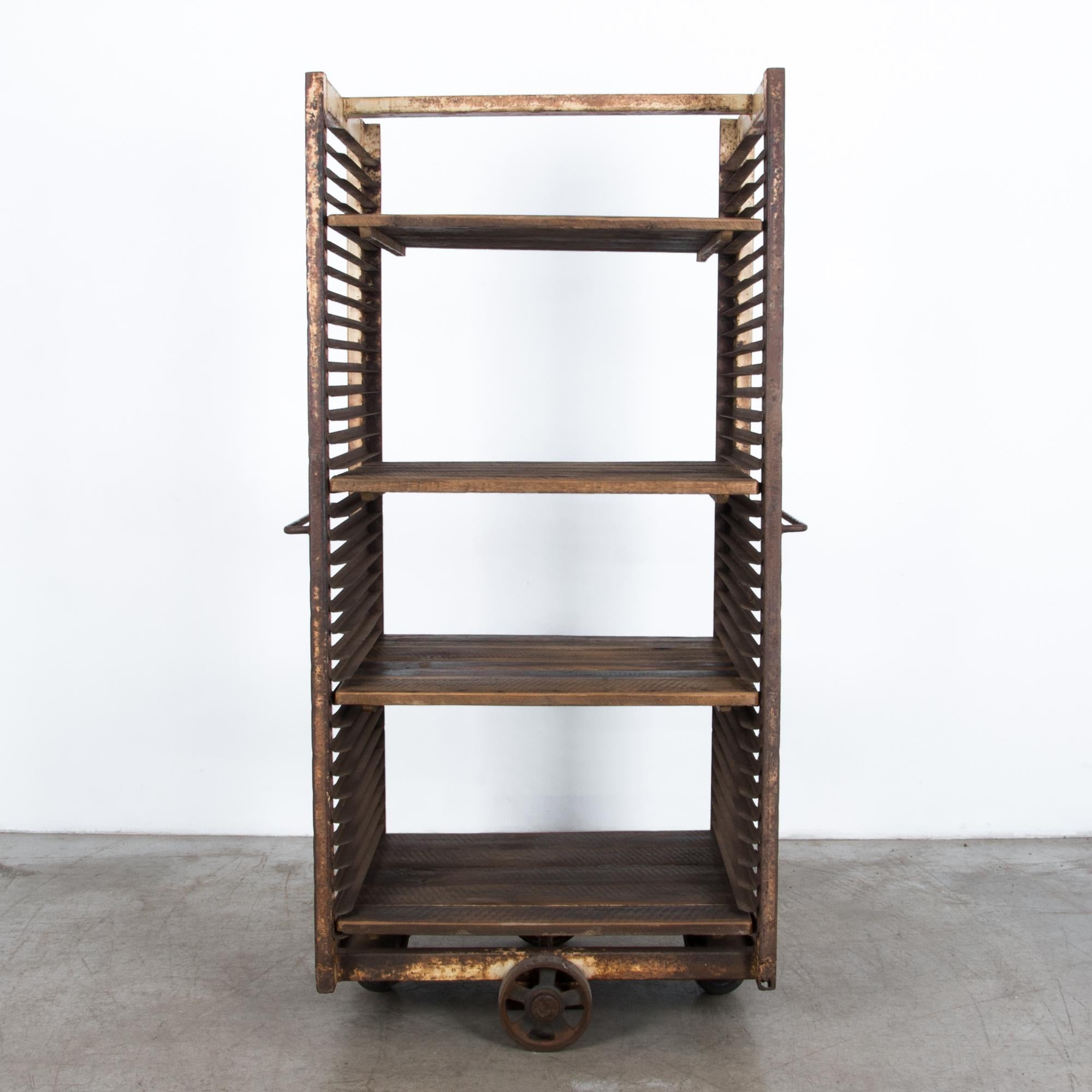 From France circa 1950, a tall wheeled iron cart with adjustable wooden shelves. With a thick textured patina worn by years of use, this shelving unit brings an industrial touch to a space needing texture.
