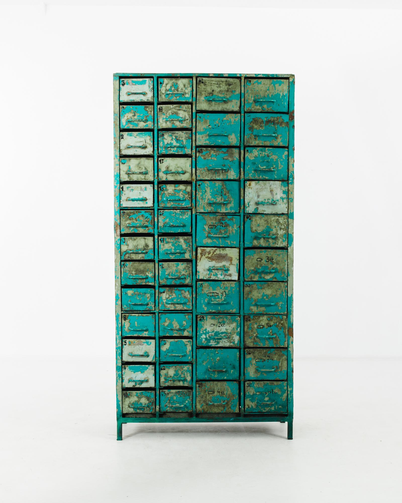 The striking patina of this filing cabinet from 1950s France lends an idiosyncratic edge to the industrial form. The original teal blue paint has been scraped and chipped away, revealing the gold and grey of the metal beneath. The distressed finish