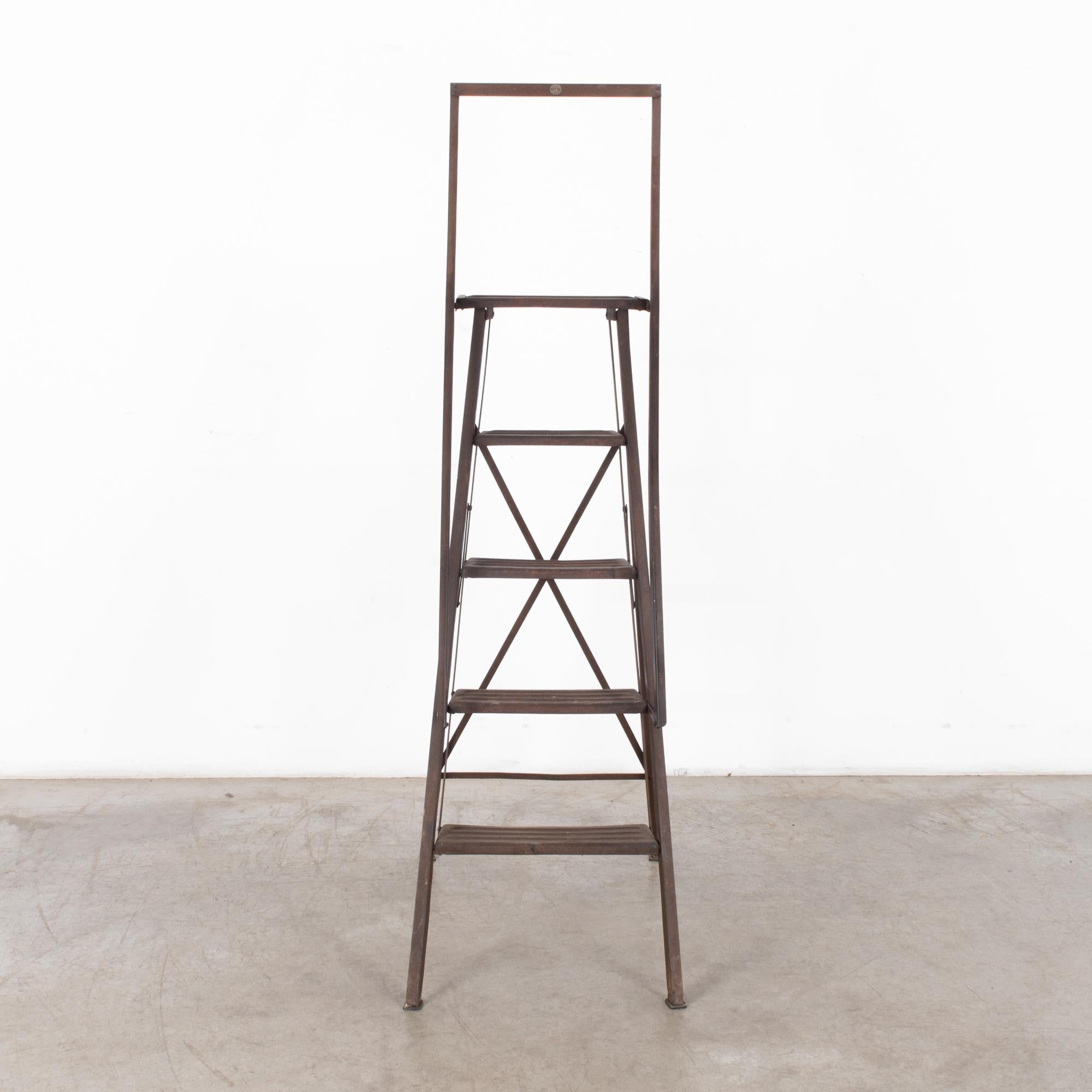 This metal step ladder was made in France, circa 1950. The rear rails have an X-frame, and long grab rails provide stability. With its dark patinated rust, the ladder will be a rustic and quaint accent in any interior.