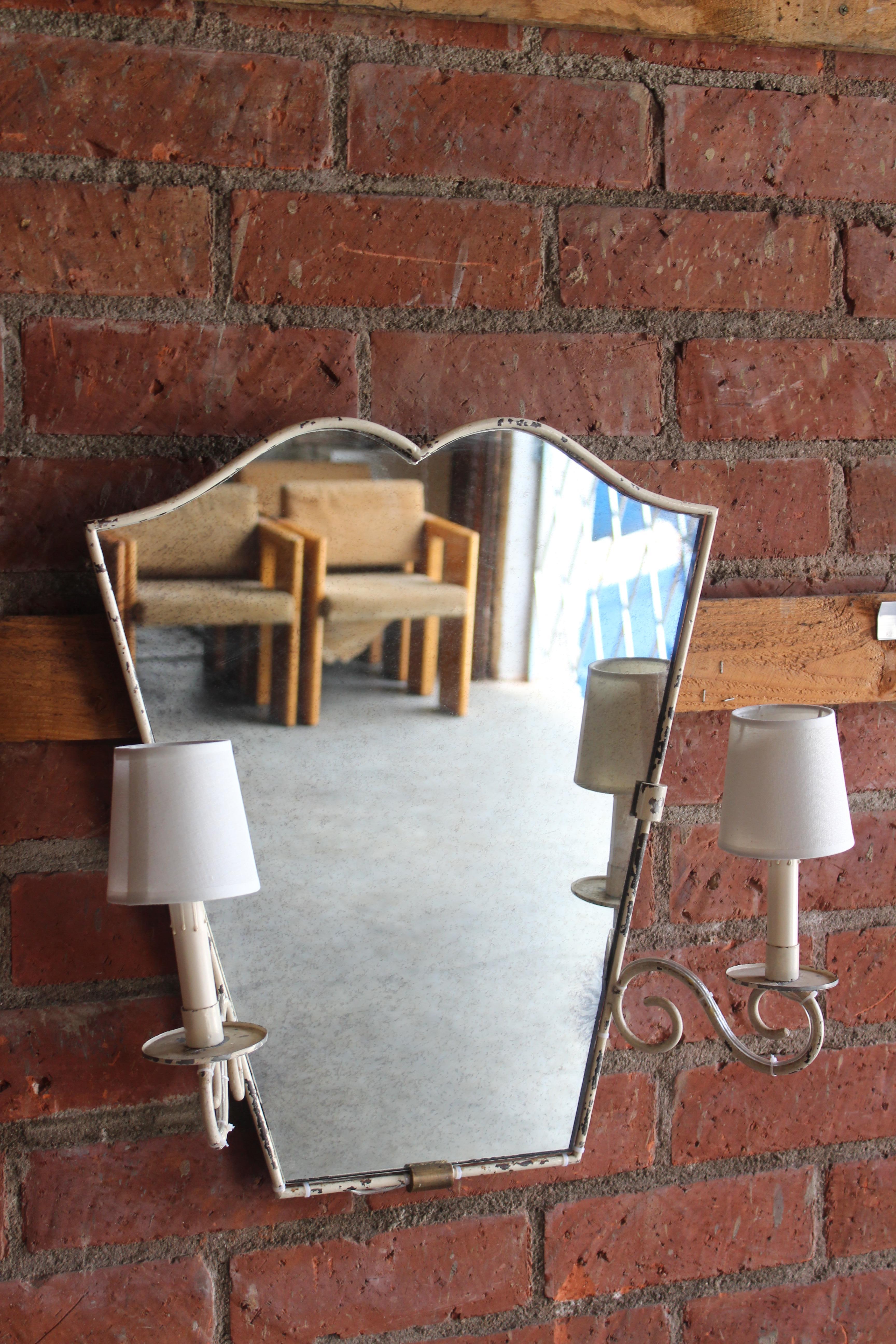 A vintage 1950s French iron wall mirror with two attached lights. In original white enamel coating which shows some wear. The mirror has been replaced with an antique mirror. Newly rewired. Uses two standard candelabra bulbs.