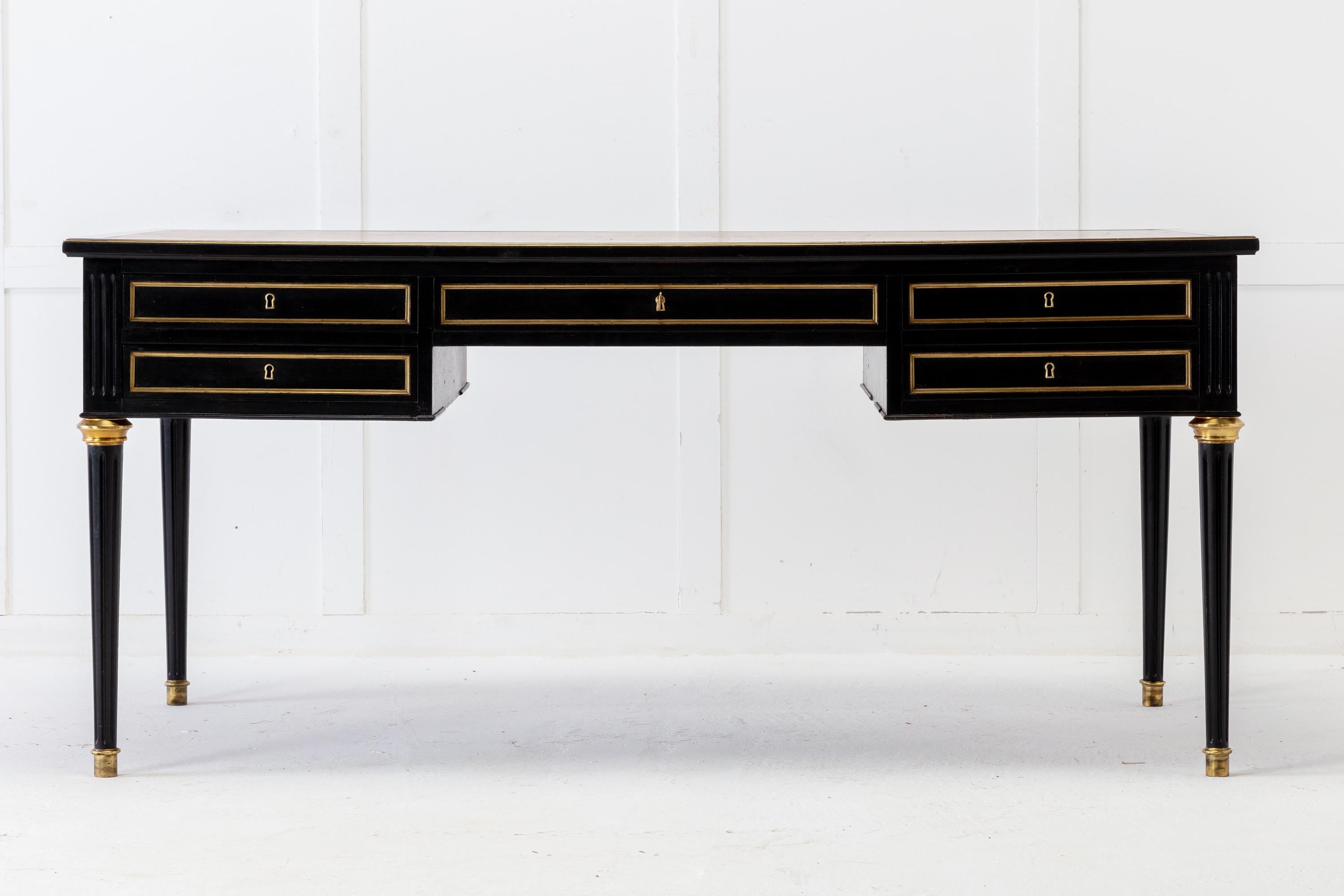 1950s French Louis XVI-style desk made of mahogany wood with a deep ebonised and lacquered finish. The top features the original embossed leather insert writing surface. There are five drawers with brass mouldings flanked by fluted tablets. Standing