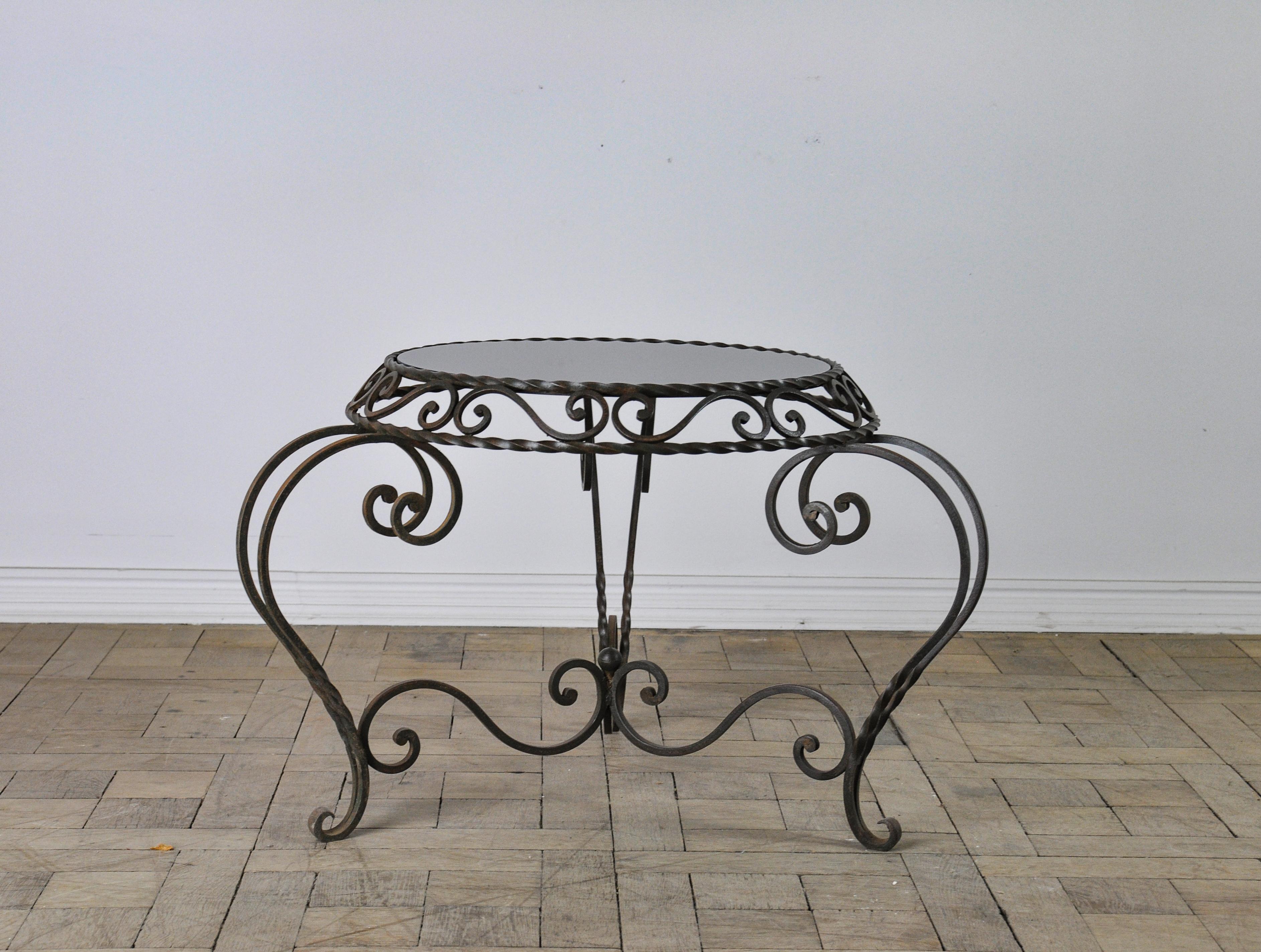 Immerse yourself in the vintage charm of this 1950s French metal coffee table, a piece that effortlessly encapsulates the spirit of its era. The table’s foundation is a symphony of wrought iron curves, intertwining to form a base as sturdy as it is
