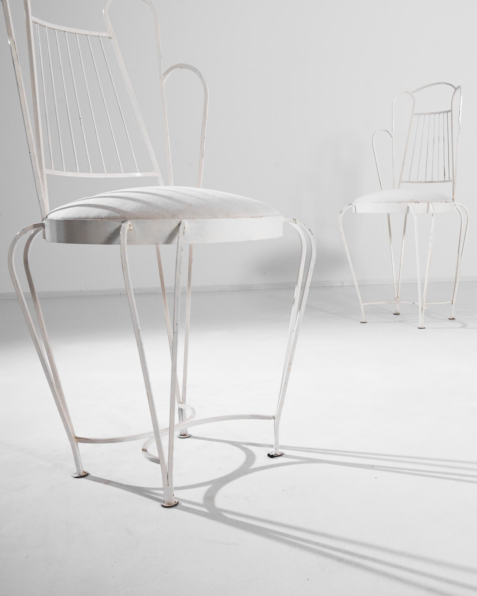A pair of metal garden chairs from 1950s France in crisp white. The sinuous design of the metal frame forms a simple yet poetic silhouette. Cabriole legs, tapering to precise points, support an upholstered circular seat, while the lyre-shaped