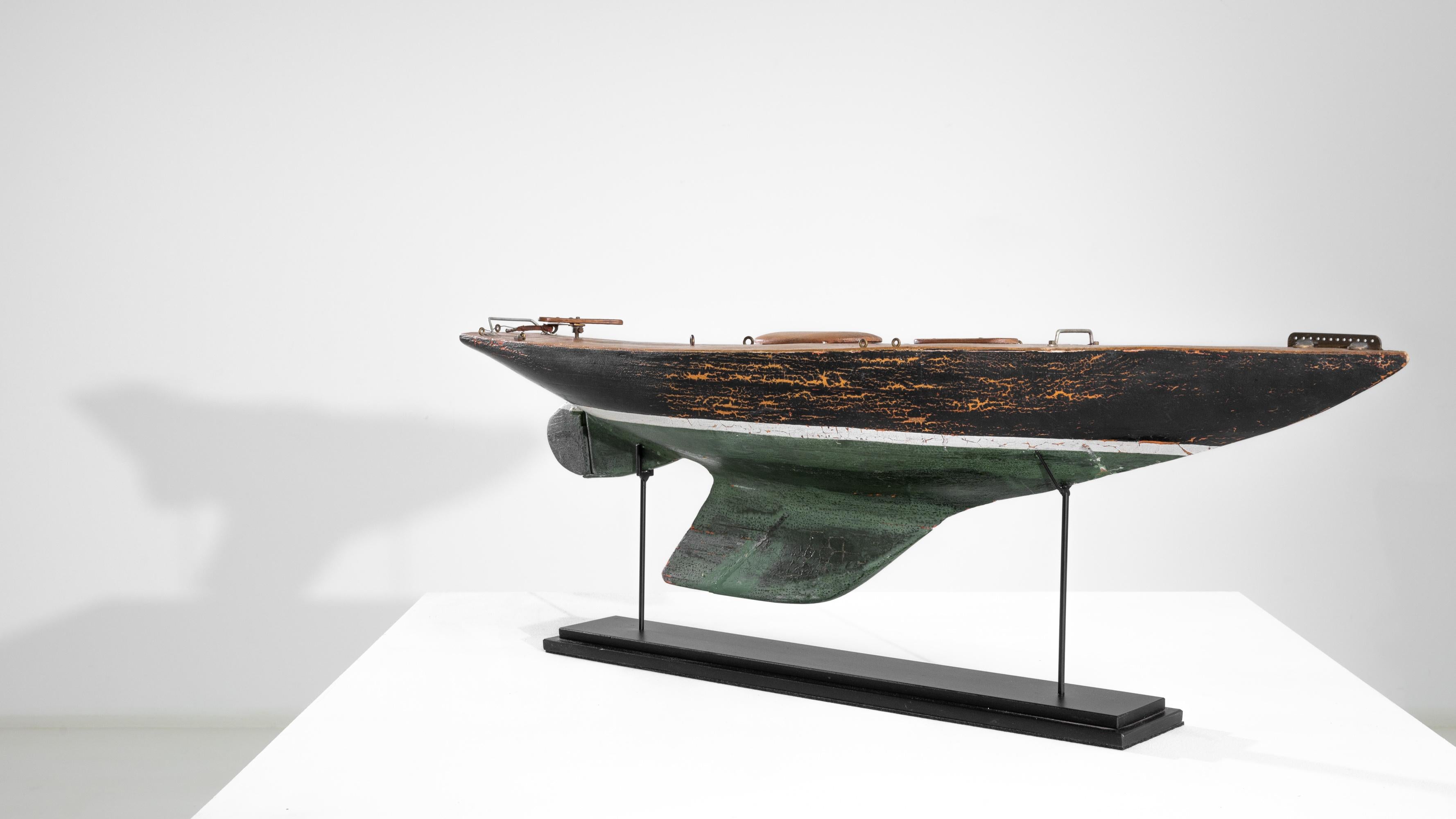 A beautiful miniature wooden boat produced in France, circa 1950. A model pond sailboat balanced on a metal stand, leans on two slender rods in an airy posture. The exterior exhibits a rich black and bottle green finish, segmented by a dainty white