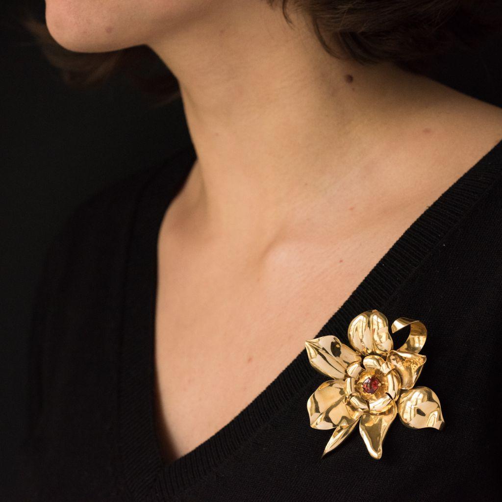 Brooch in 18 karat yellow gold, eagle head hallmark. 
In the form of a flower, the centre is set with an oval orange garnet cabochon. The closure is a double pin. 
Height: 7.3 cm, width: 6.8 cm.
Total weight : 34.8 g.
Authentic vintage brooch –