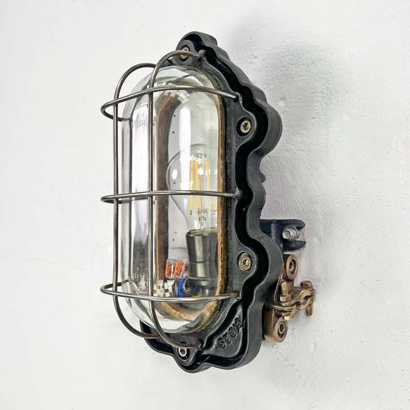 A black mild cast steel vintage bulkhead wall light by Perfeclair Paris with thick glass cover which has the company logo embossed onto it. This is an indoor wall light with protective cage ideal for robust use and modern, rustic or industrial style