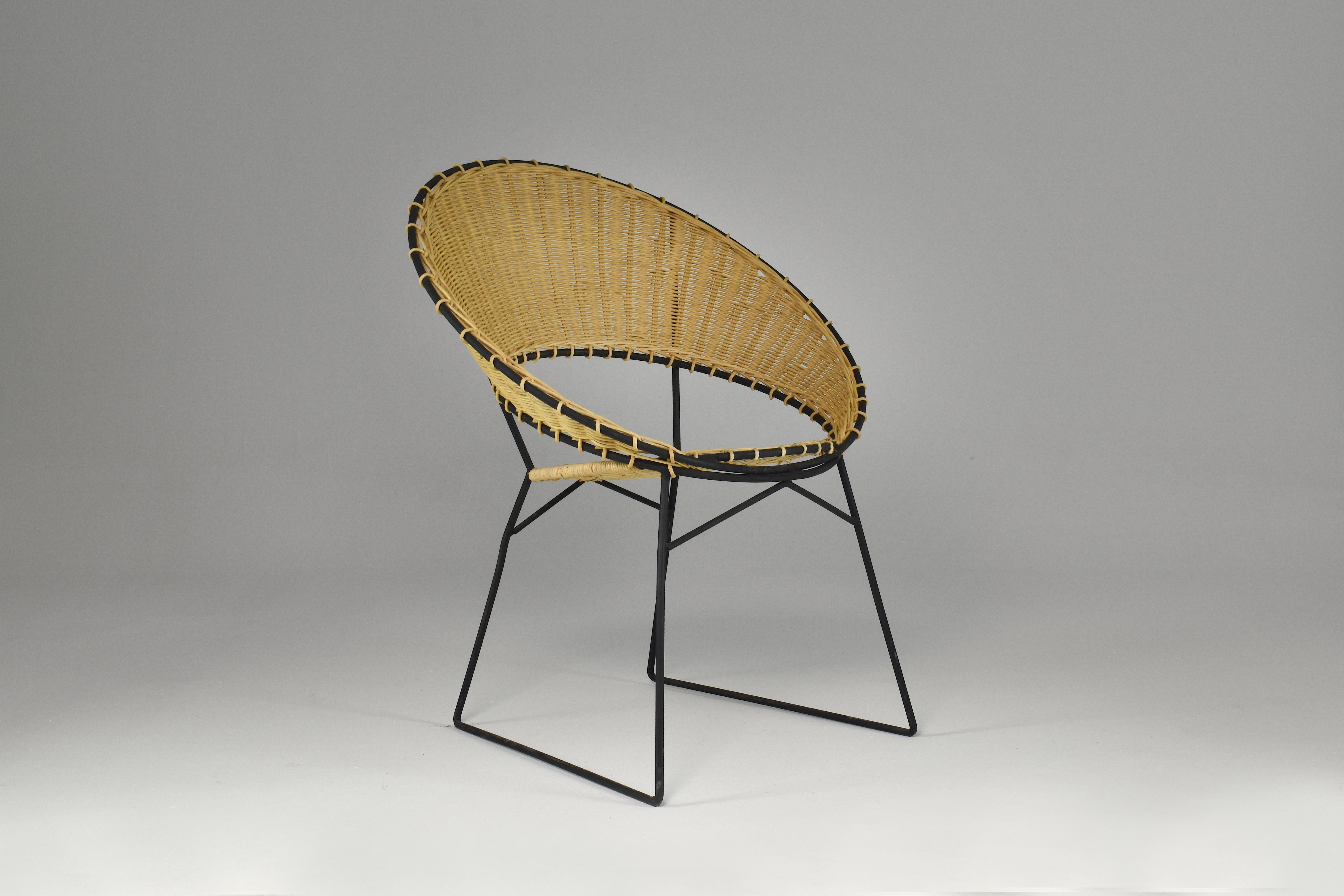 A fantastic 20th-century vintage armchair and side table with magazine rack set designed by French decorator Raoul Guys in the 1950s. Both designs are made of rattan and tubular black lacquered steel. 
The structure and rattan are in entirely