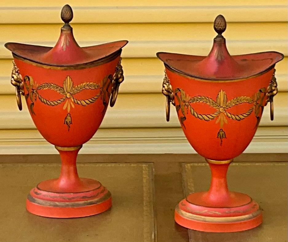 This is a pair of French neo-classical style toleware urns. They are gilt painted on a Hermes orange. They are signed and in good condition with lite wear.