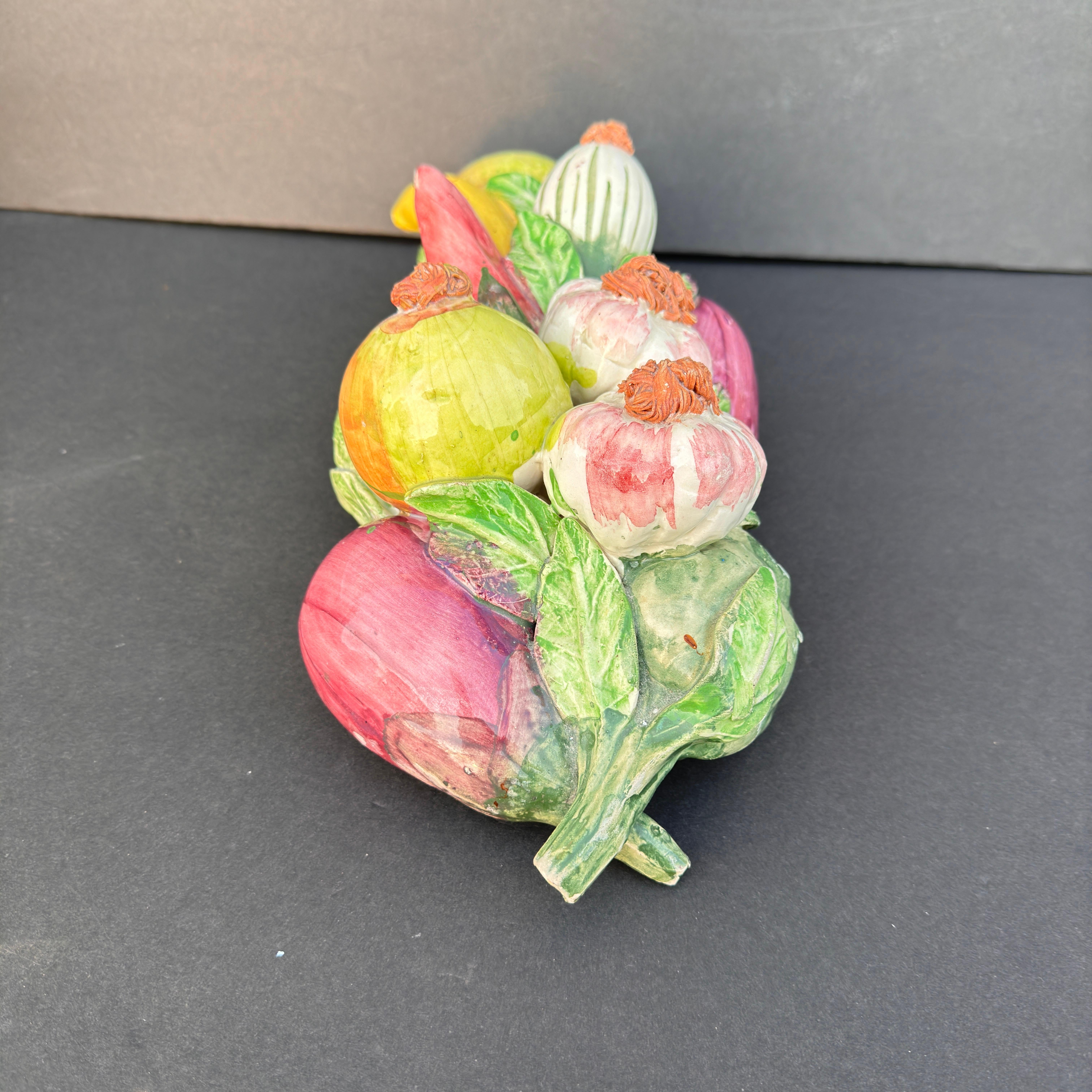 Este singular arreglo cerámico de verduras de colores es un complemento encantador y vibrante para las  cocinas o encimeras. Con un hermoso surtido pintado a mano, que incluye bulbos de ajo, cebollas, calabazas y berenjenas, la pieza desprende una
