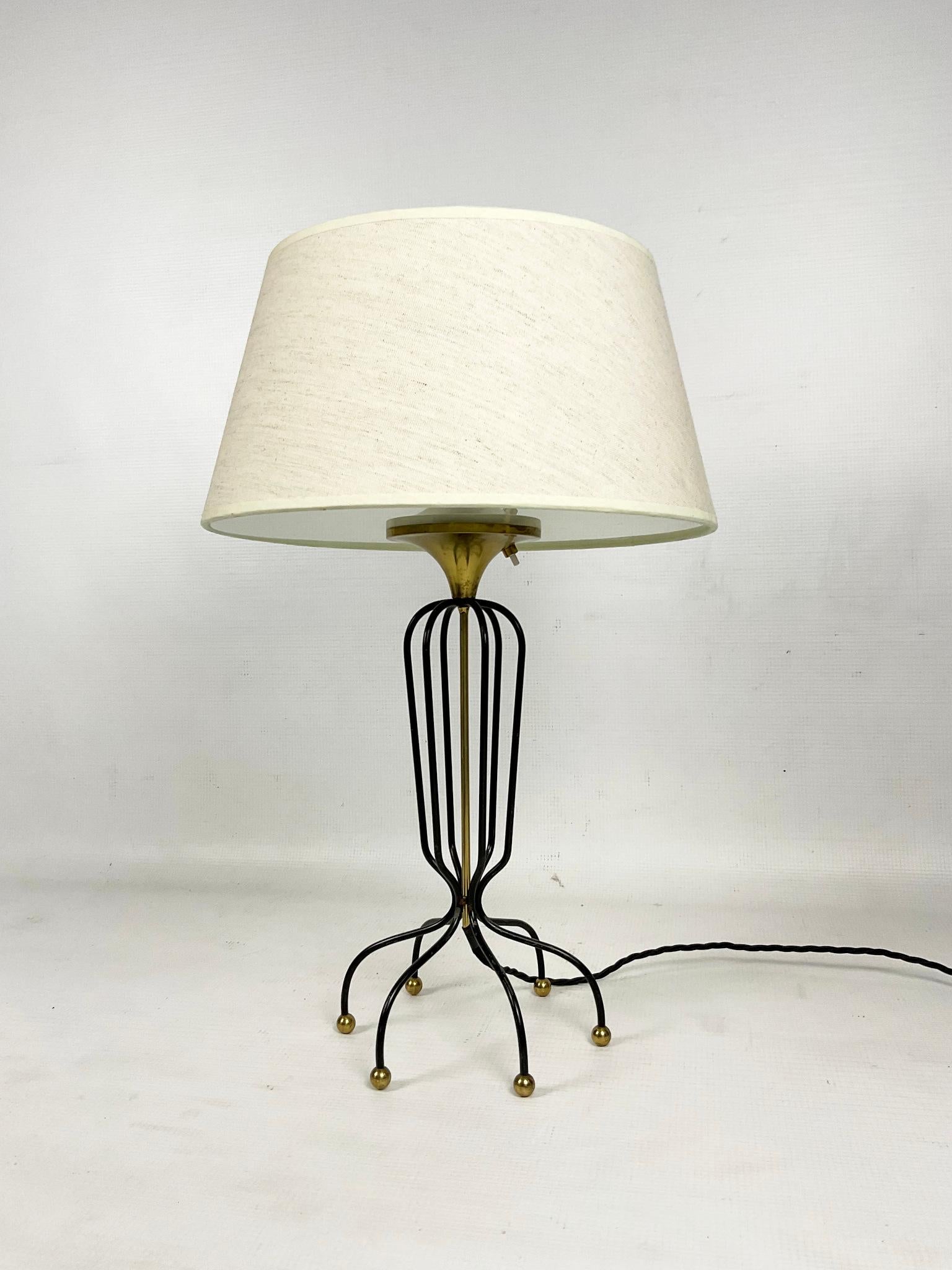 This rare 1950s table lamp was manufactured and produced by Maison Arlus France.
The lamp is composed of a thin brass column surrounded by black metal rods forming the body of the lamp, with an octopus-shaped lamp base, ending in polished brass