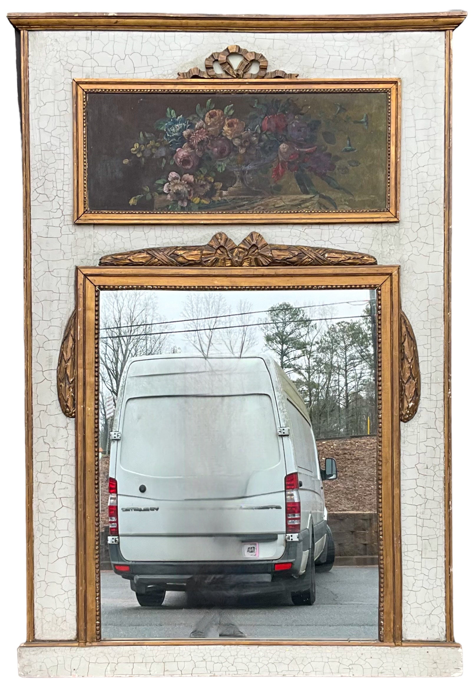 This is a 1950s French Louis XV style trumeau mirror with an ivory painted frame and carved draped giltwood foliate. The painting is a floral oil on canvas. It is in very good condition. 