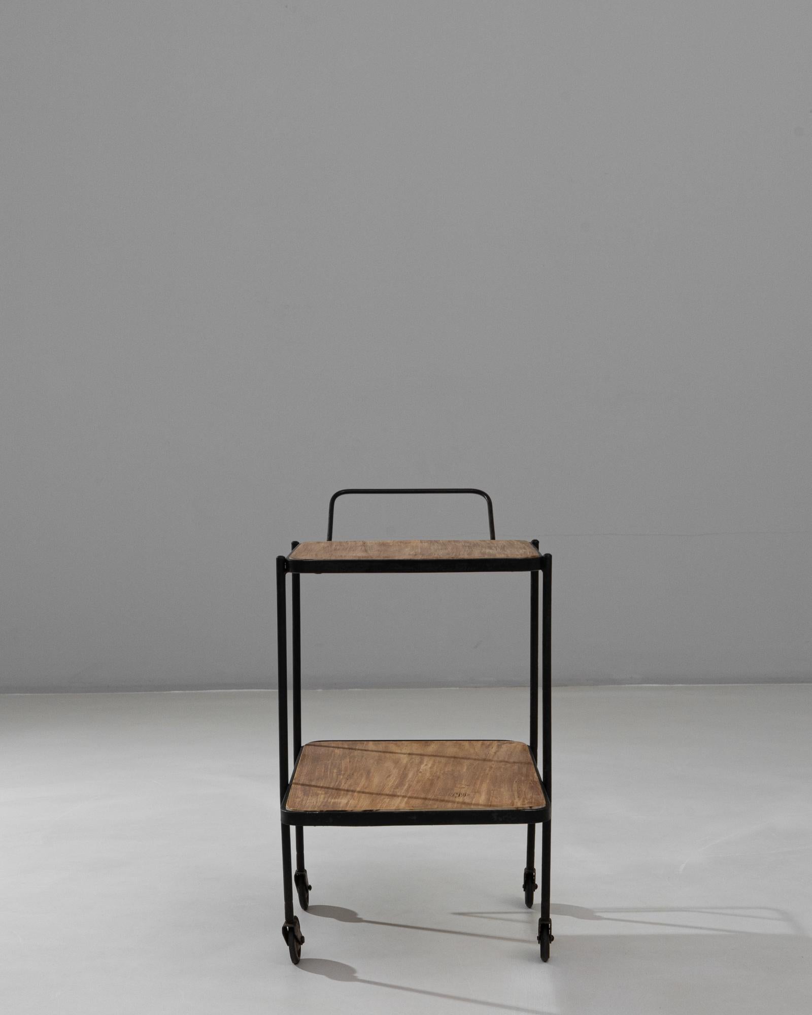 This 20th Century French rolling side table blends industrial simplicity with subtle handcrafted charm. The design features two oak shelves with a warm, natural finish, each framed by a slim black metal edge that adds structure without overpowering
