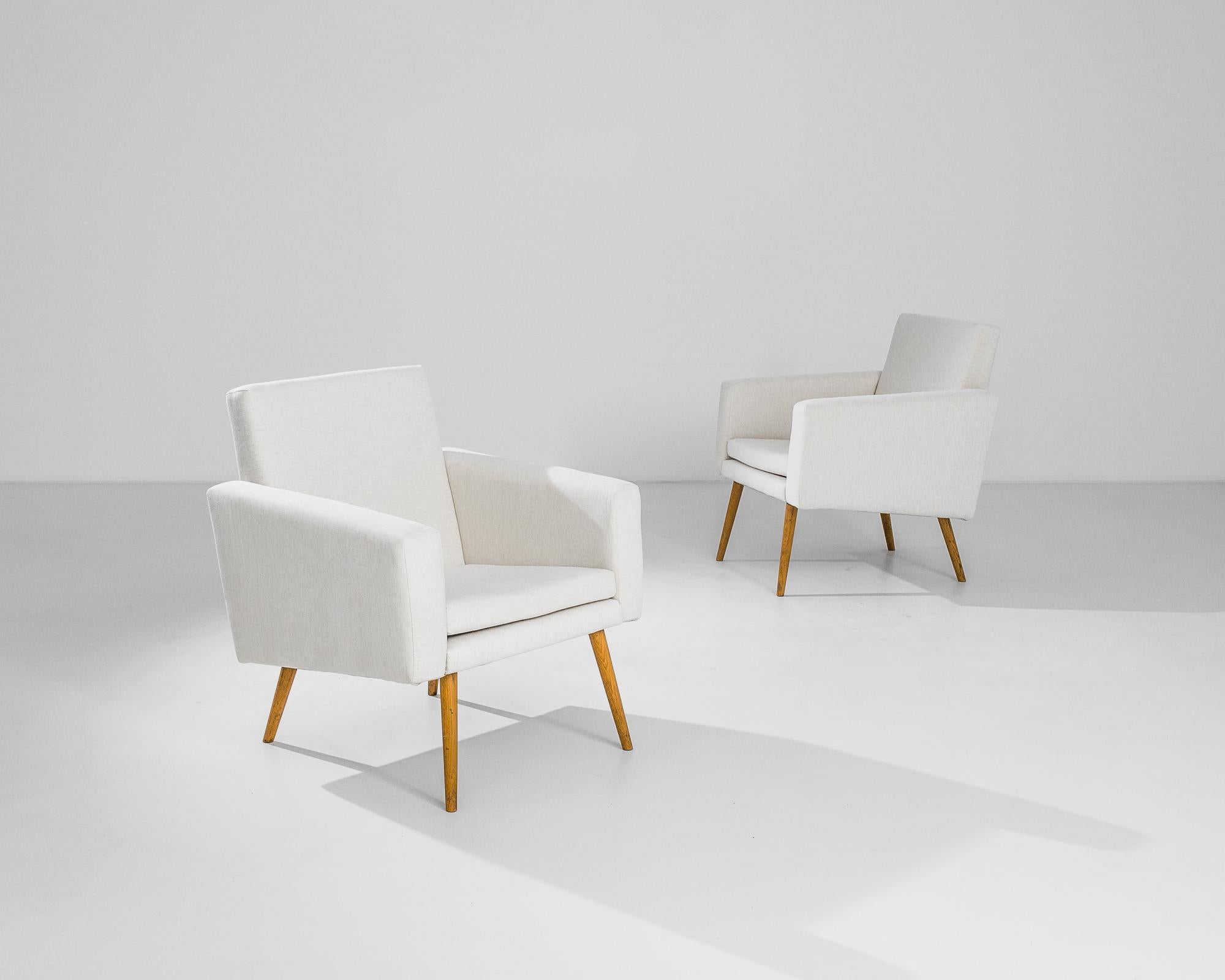 Clean, graphic and sophisticated, this pair of vintage armchairs possess a unique Minimalist silhouette. Made in France in the 1950s, tapered wooden legs offer an agile counterbalance to the boxy profile of the upholstered seat; the angles of the
