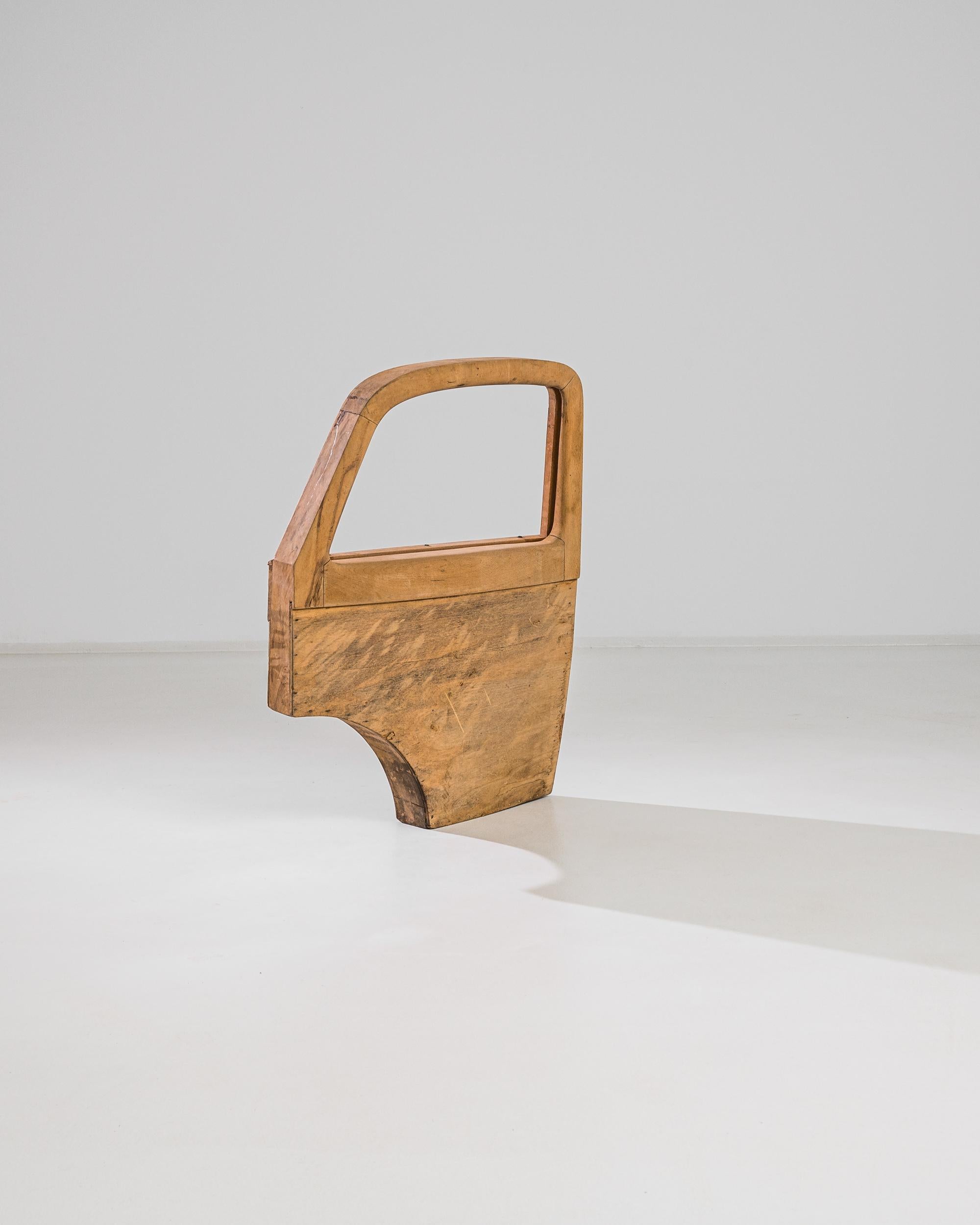 A decoration from 1950s France in solid beech and plywood. The graphic silhouette, reminiscent of the door of a vehicle, evokes the streamlined shapes of the golden age of car design. The open, window-like space creates a natural frame, accentuating