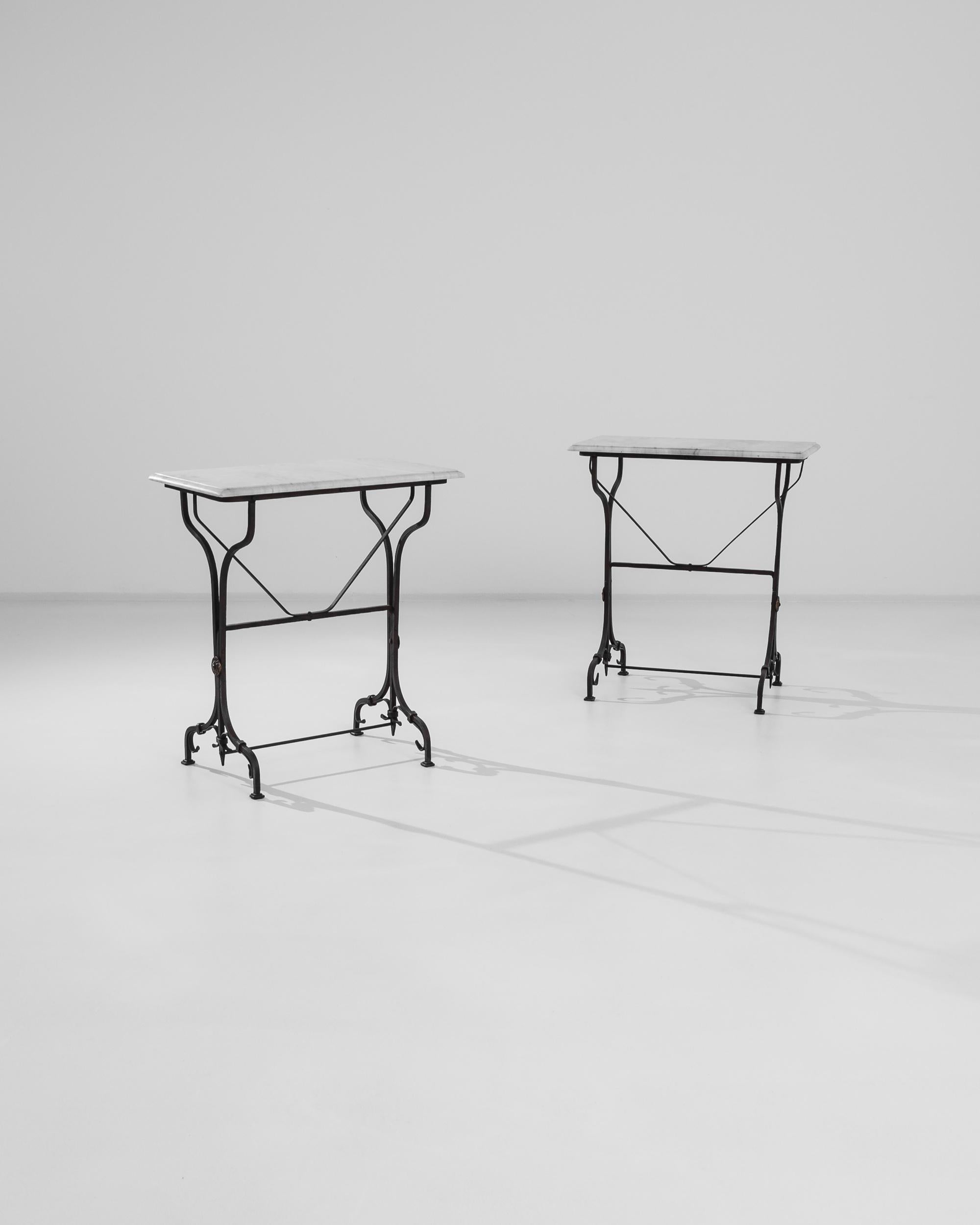 This pair of wrought iron tables from 1950s France provide a unique and eye-catching accent. The dark metal of the frame creates a striking silhouette; railheads and curving decorative bars add a sinuous gothic touch. A tabletop of white marble,