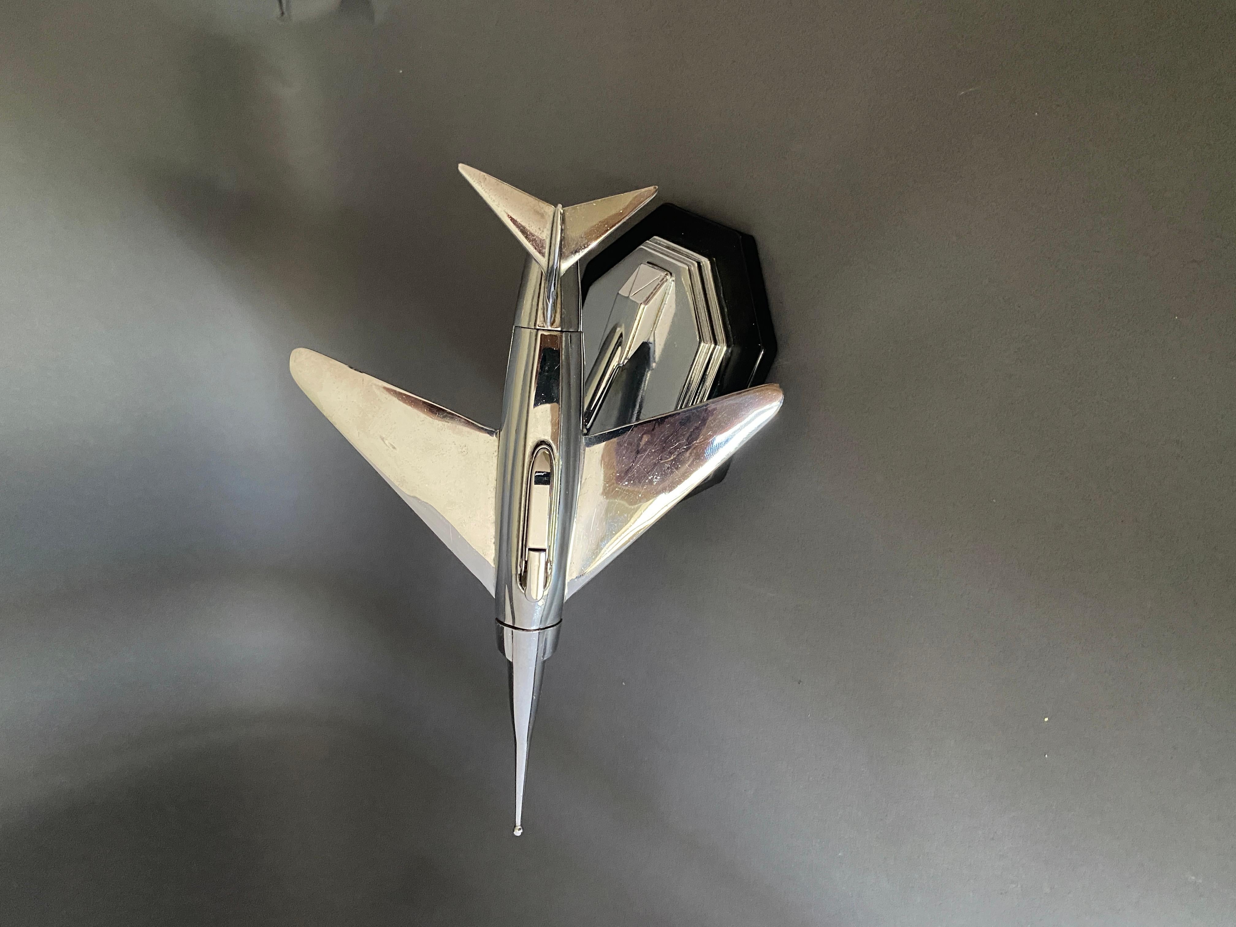Briquet de table vintage chromé, en forme d'un 
 Avion de chasse circa 1950
Allume-cigarette encastré dans le corps de l'avion, [prise de balle].
Support stylisé pour maintenir la boule pivotante, pour montrer l'avion de chasse dans le ciel. 
de