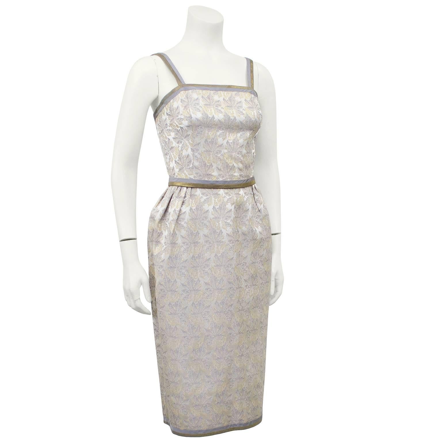 Extremely beautiful 1950s Galerias Preciados wriggle style cocktail dress. Metallic silver with gold and pewterr brocade leaf pattern. Greyish silver and bronze/gold trim at straps, neckline, belt and hem. Fitted bodice, cinched waist with removable