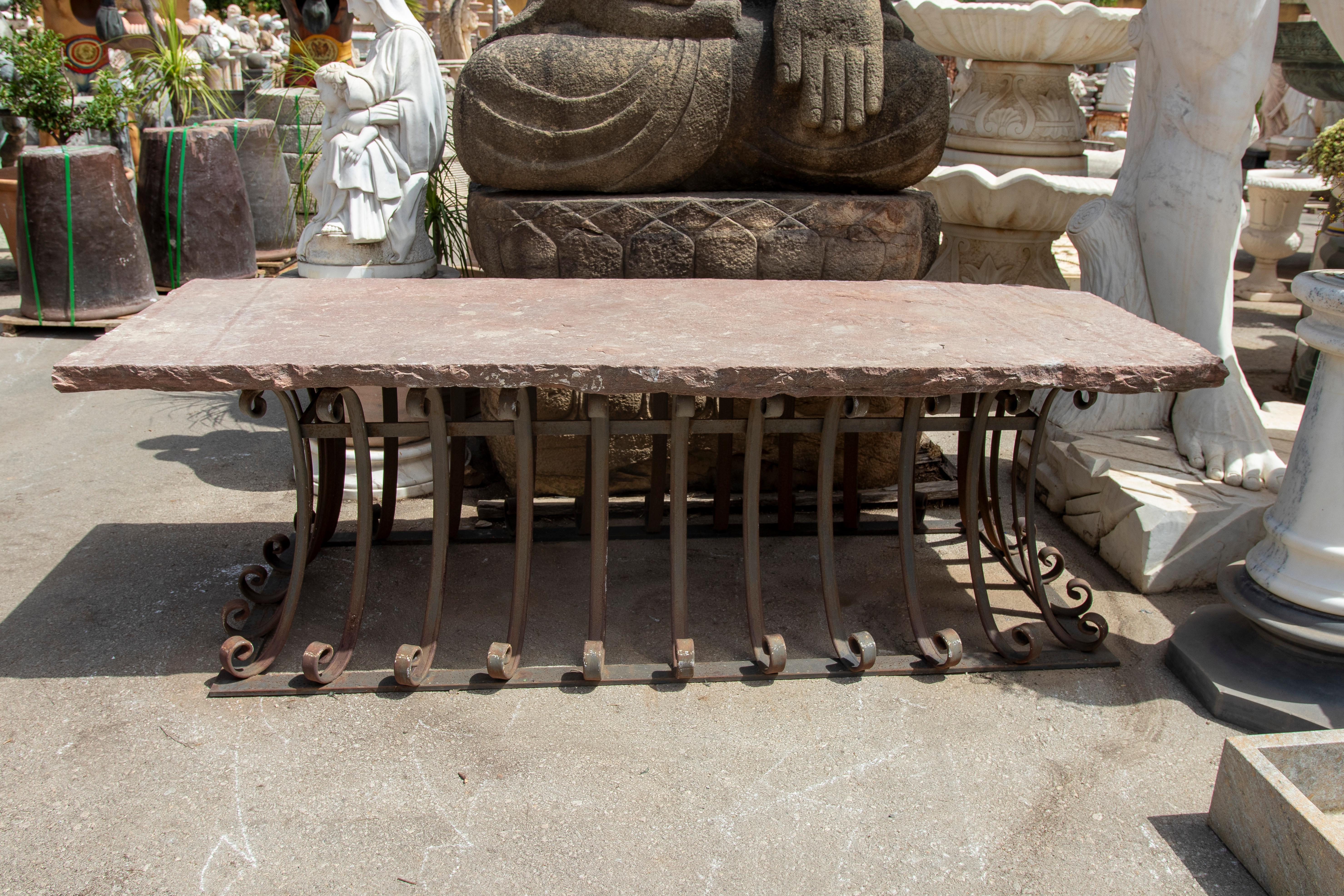Esta elegante mesa de exterior combina la solidez de una gruesa losa de piedra natural con la sofisticación de una base de hierro forjado artesanal, creando una pieza robusta con una estética impactante. El tablero de piedra, con un acabado rústico