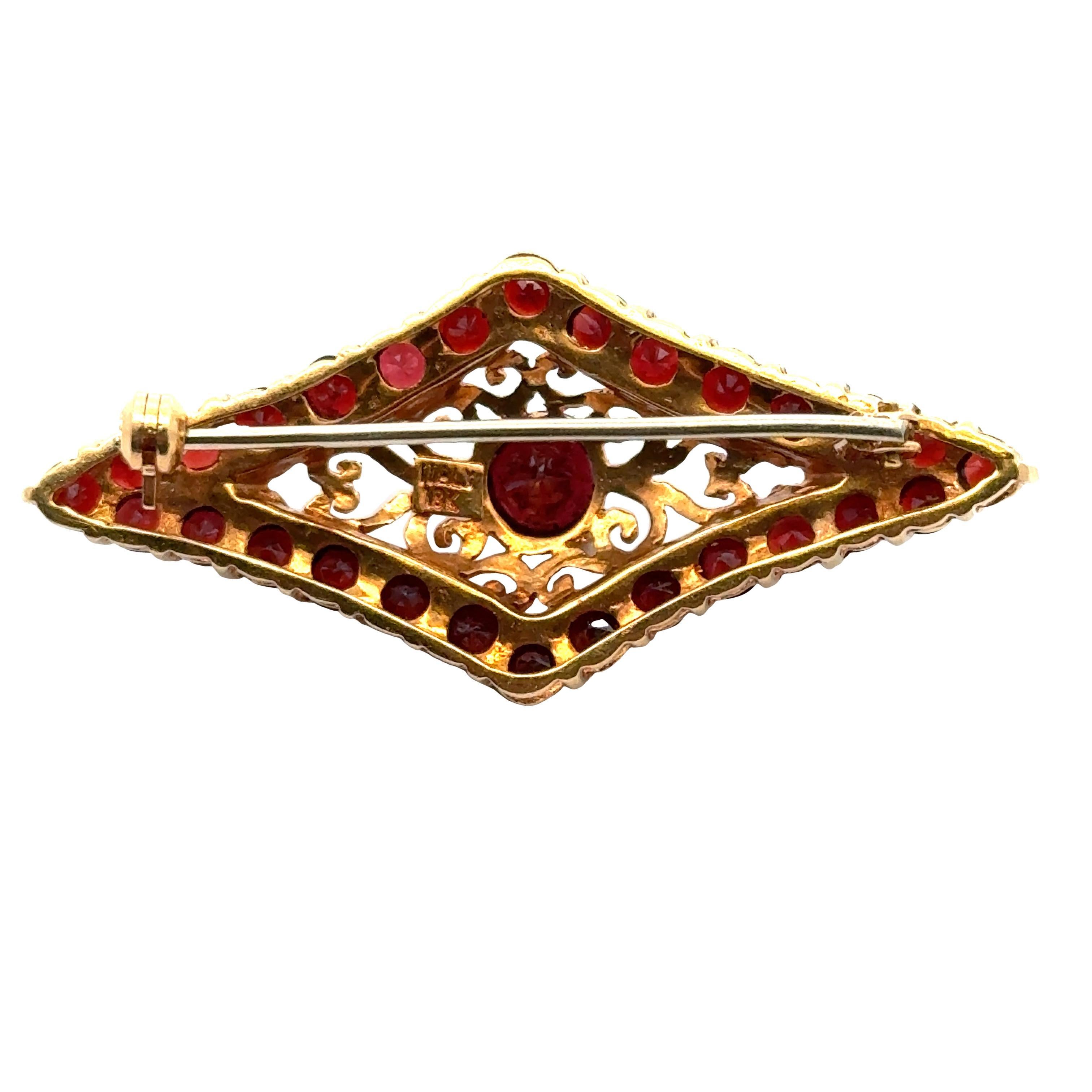 1950's garnet gemstone brooch handcrafted in 18 karat yellow gold. The decorative textured gold brooch features round garnet gemstones outlining the piece and one set in the center. The pin measures .75 x 2.00 inches. Weight:8.9 grams.