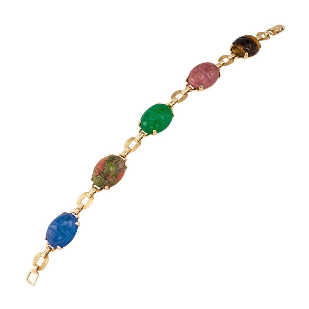 1950s scarab gold bracelet by Engel Brothers. Comprising a series of five oval scarabs carved from, starting at left, tiger eye, rhodonite, green onyx, unikite and blue chalcedony, mounted in 14-karat yellow gold with maker's marks for Englel