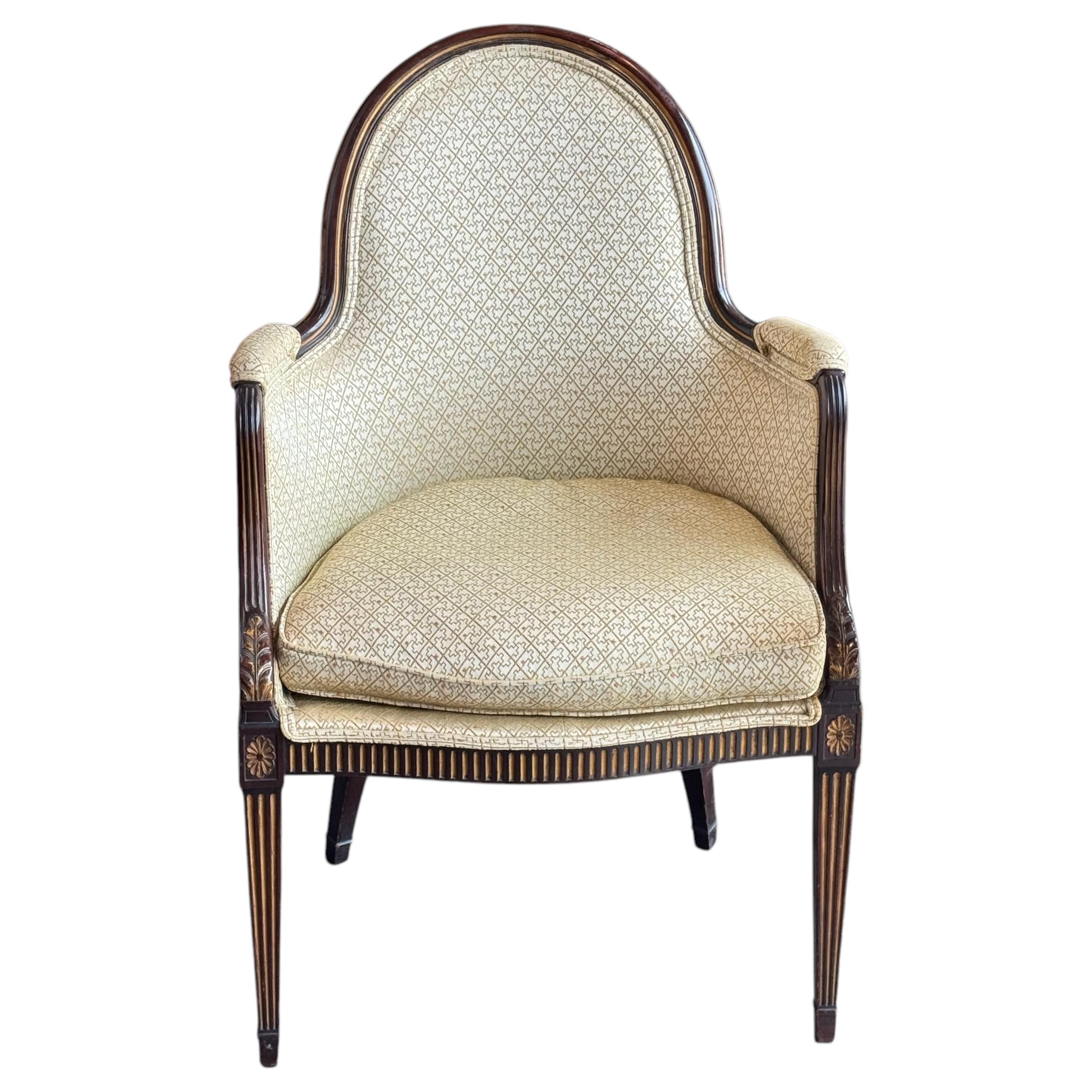Elegante sillón de estilo Jorge III con armazón acanalado con rosetas talladas en las esquinas y patas cónicas. La madera luce un fino junquillo y un acabado oscuro que contrasta con la tapicería estampada en color oro pálido. El respaldo curvado y