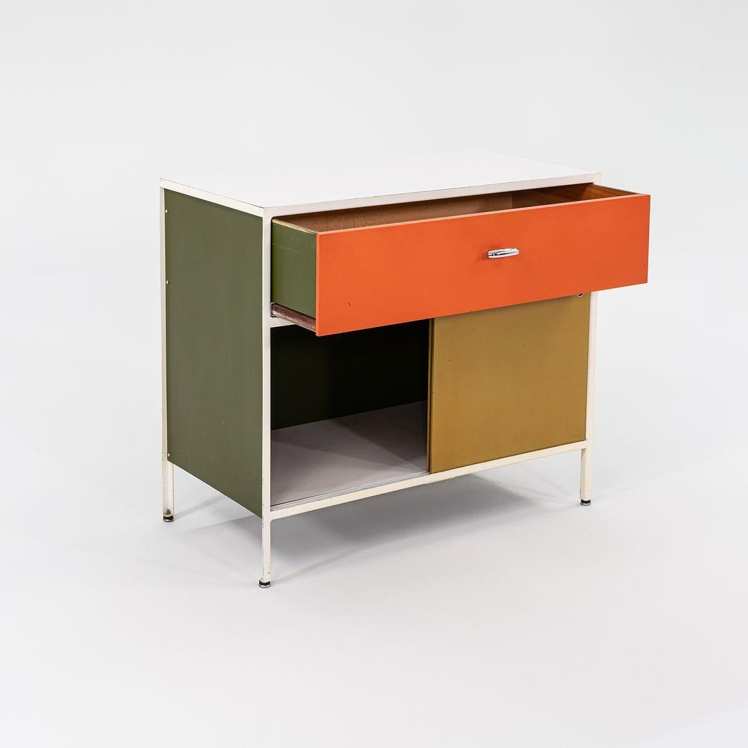 This is a Steelframe No. 4000 Series Cabinet, initially designed by George Nelson for Herman Miller in 1950. Its model number is 4033. It features a frame of white powder-coated bent iron, olive green Masonite side panels, and features one drawer