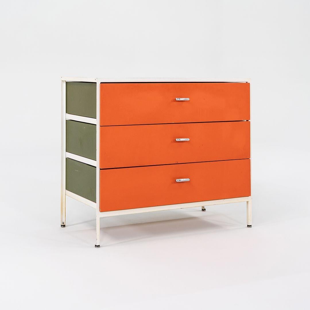 This is a Steel Frame No 4000 Series Dresser, initially designed by George Nelson for Herman Miller in 1954. Its model number is 4013. It features a frame of white powder-coated bent iron, olive green Masonite side panels, and orange steel drawers.