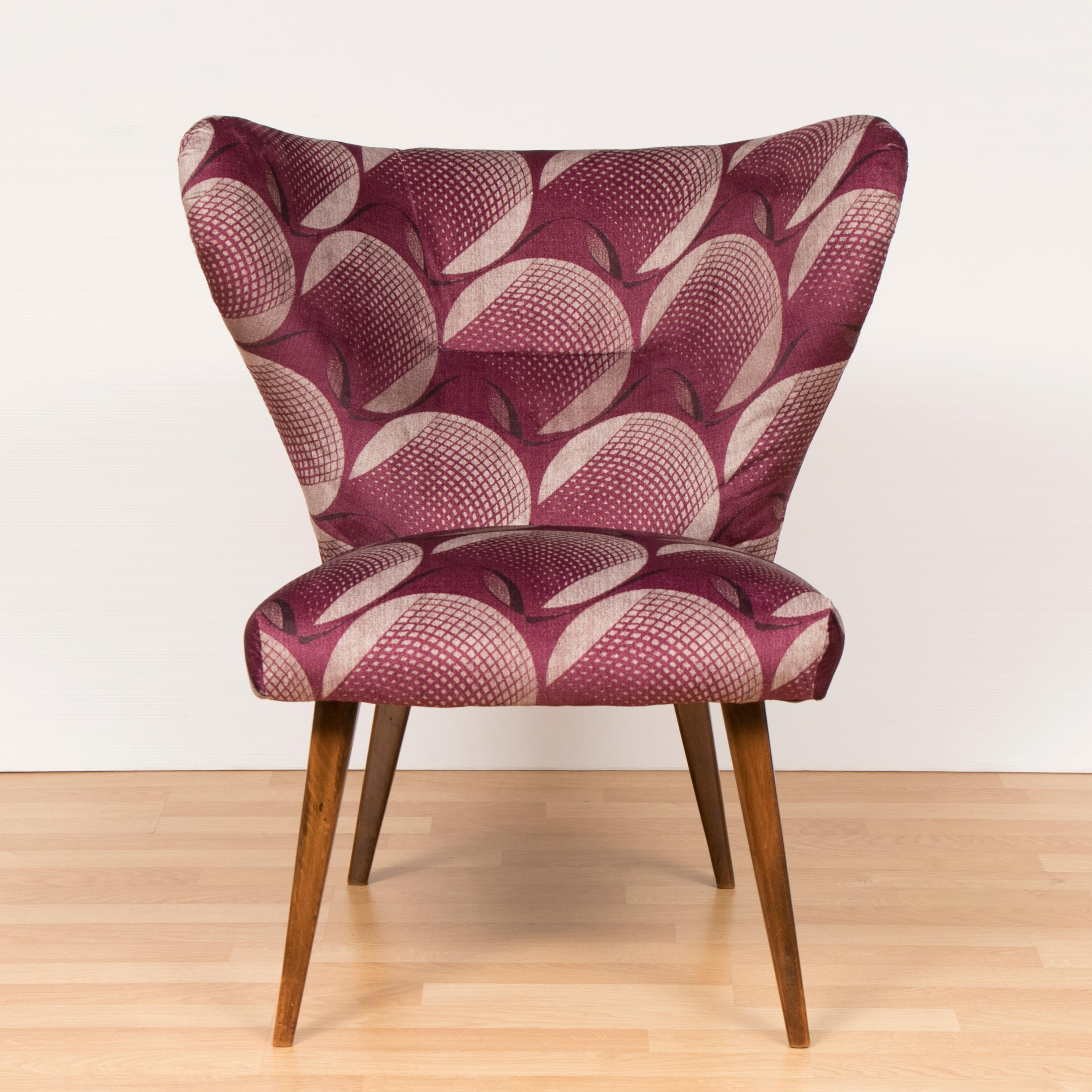 A 1950s midcentury cocktail chair newly reupholstered in vintage style fabric by Arley House. The chair has large stylized wings which support and curve around one's back. The chair sits on newly restored tapered wooden legs. A feature chair