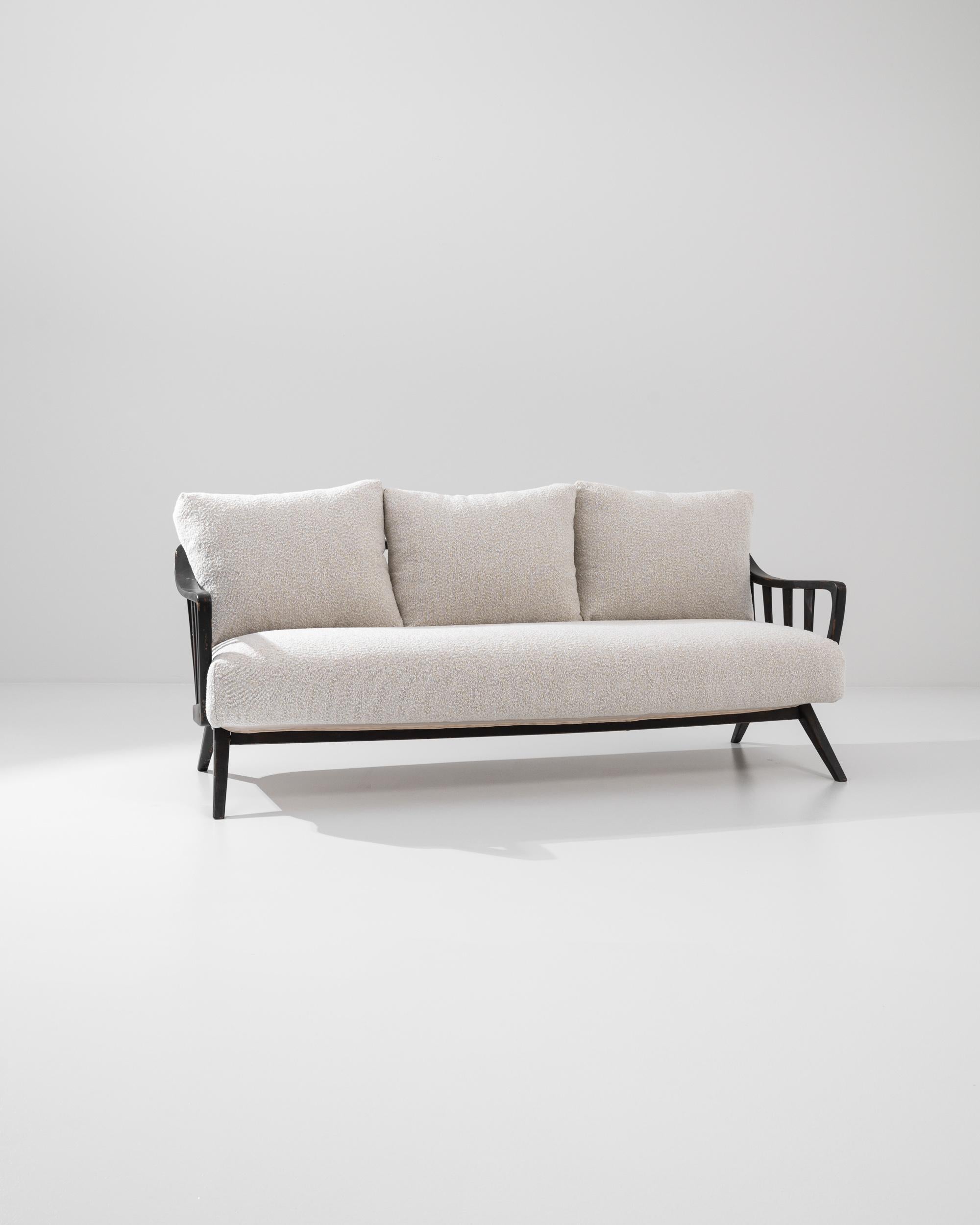 Simple and elegant, this vintage sofa combines the lyrical shapes of Biedermeier furniture with a graphic Modernist twist. Made in Germany in the 1950s, harp-shaped armrests frame the generous pillows of the seat; the clean angles of the legs