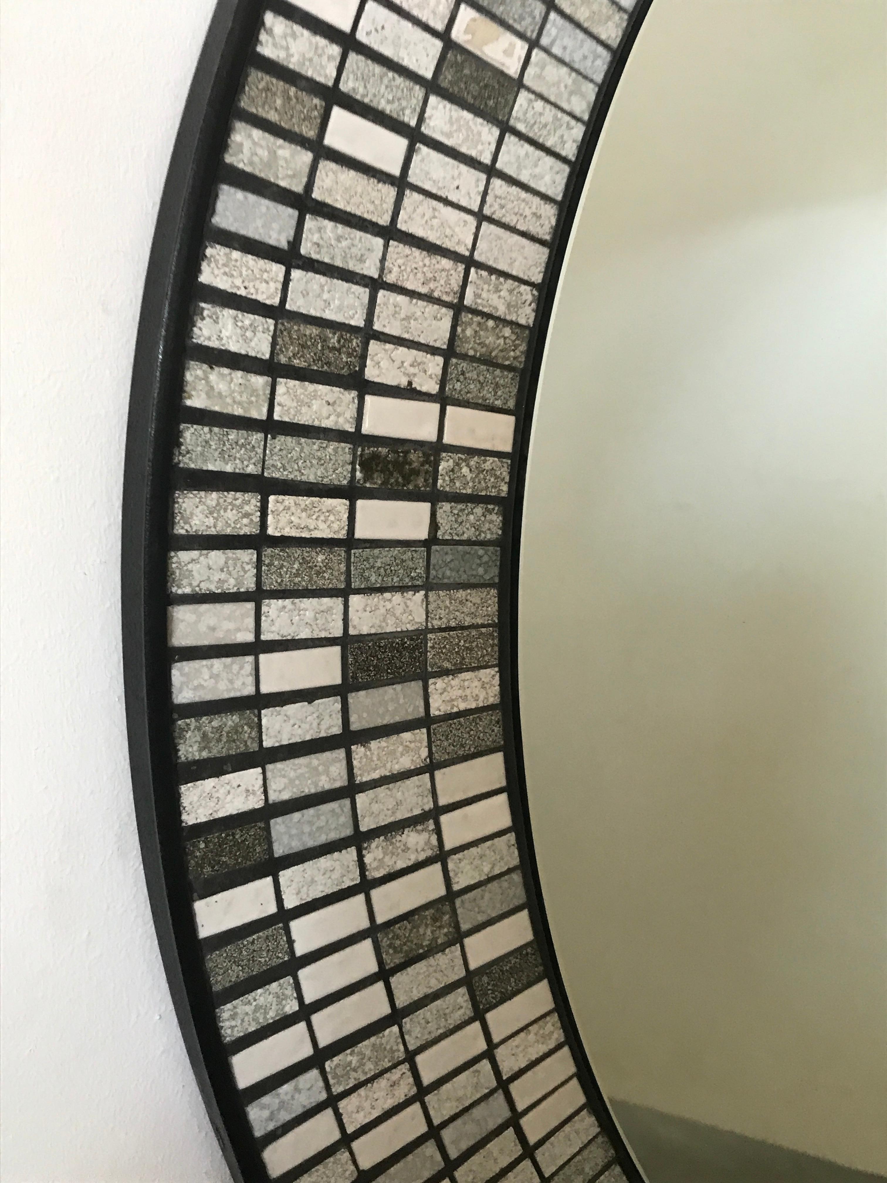 A beautiful 1950s German round mosaic wall mirror in the manner of Berthold Muller with black, gray, and white ceramics in a black metal cast.